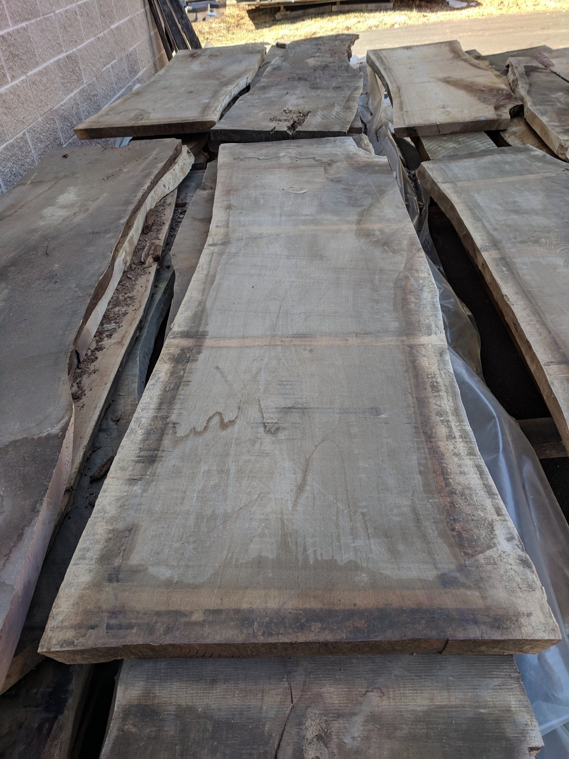 Wooden slabs, various sizes, arranged outdoors, weathered grey-brown, live edges.