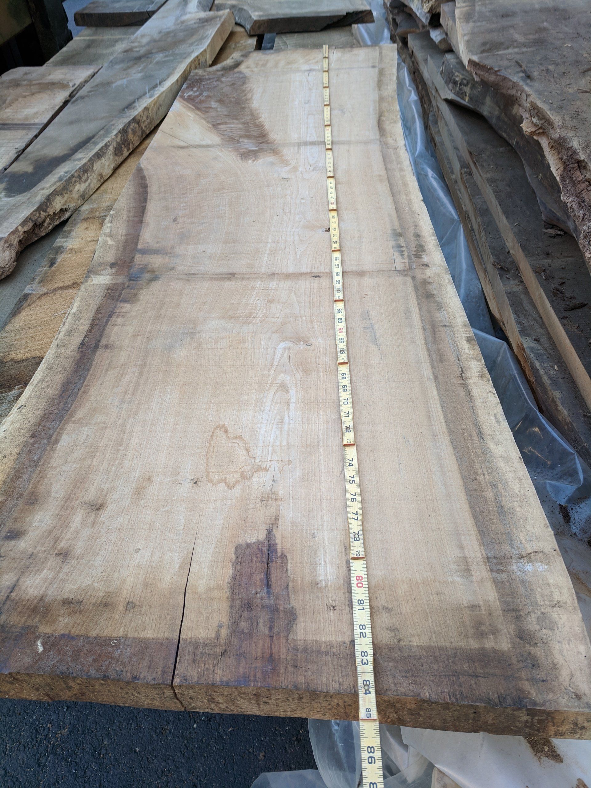 A large, light-colored wooden slab with a measuring tape running down the center. Edges are rough.