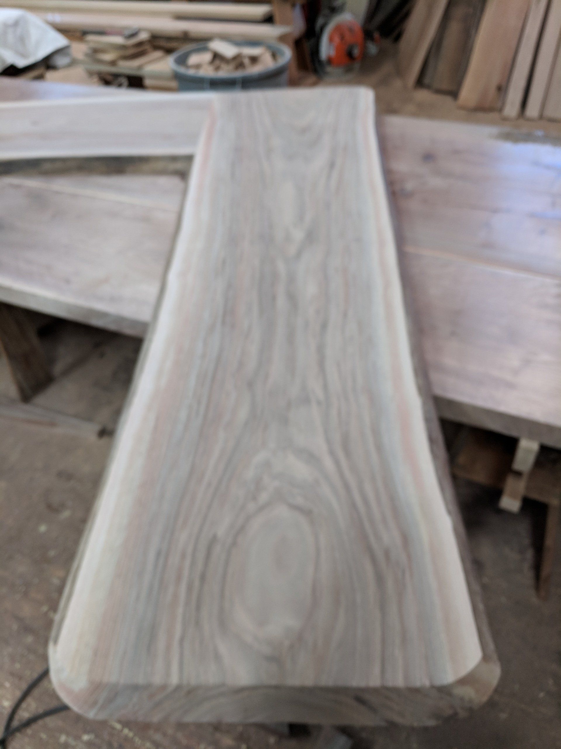 Close-up of a live-edge wooden board with a smooth, gray-toned surface and curved edges, likely for furniture.