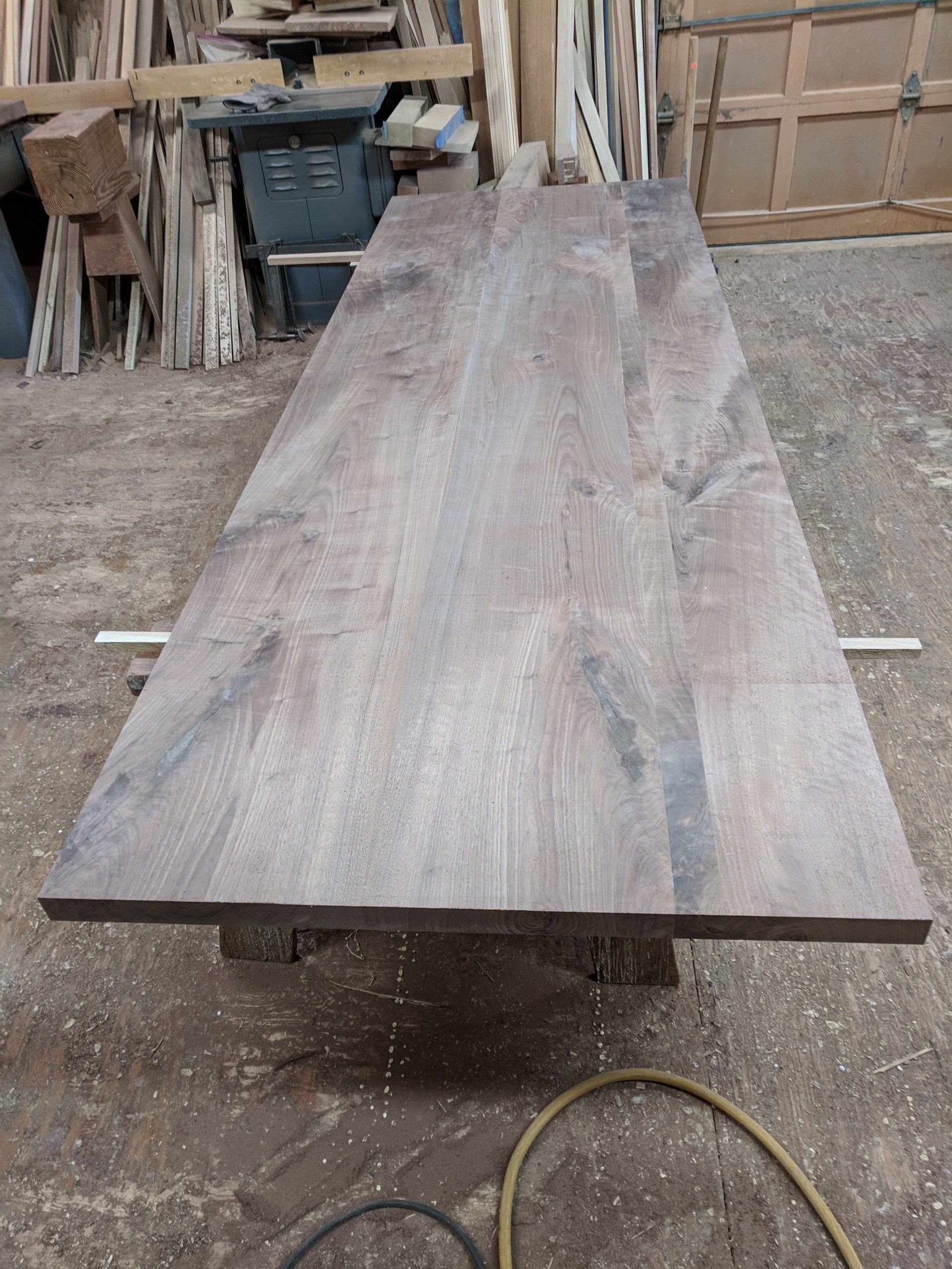 Large, rectangular wooden table top, grey-brown, resting on supports in a workshop.