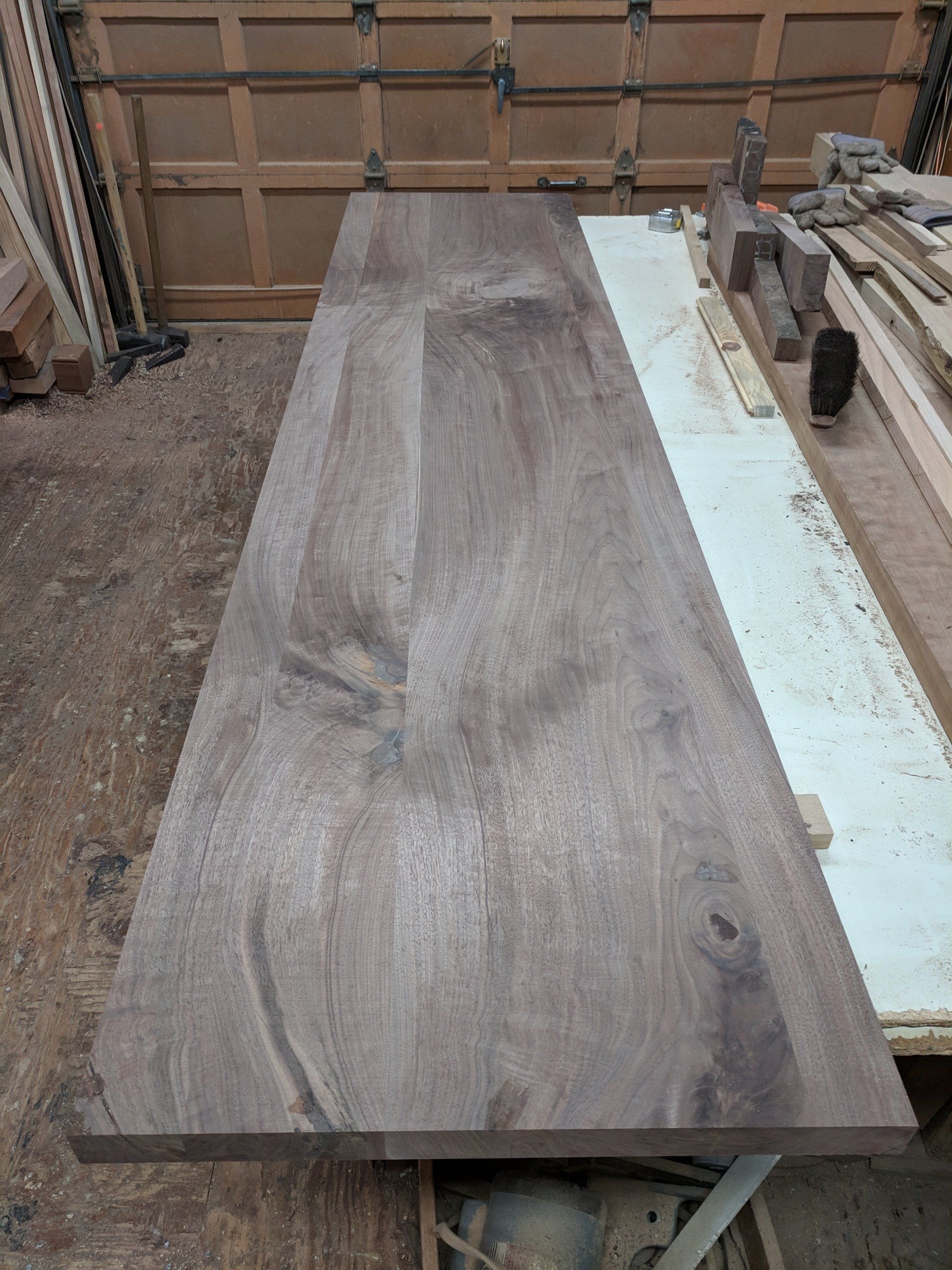 Large, dark wooden slab on a workbench. Wood grain visible. Workshop setting.