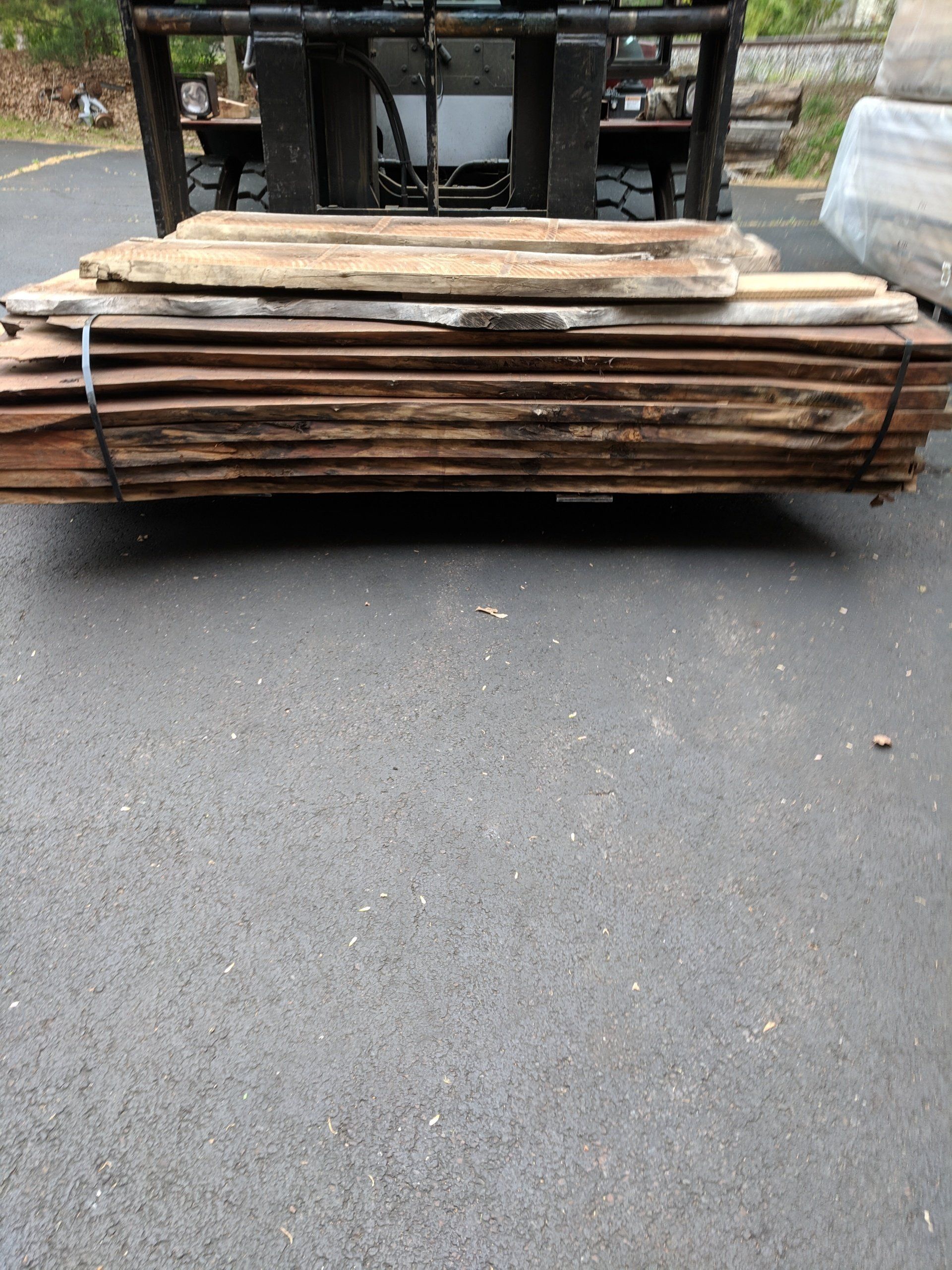 A stack of weathered wood planks secured with black straps, on a forklift.