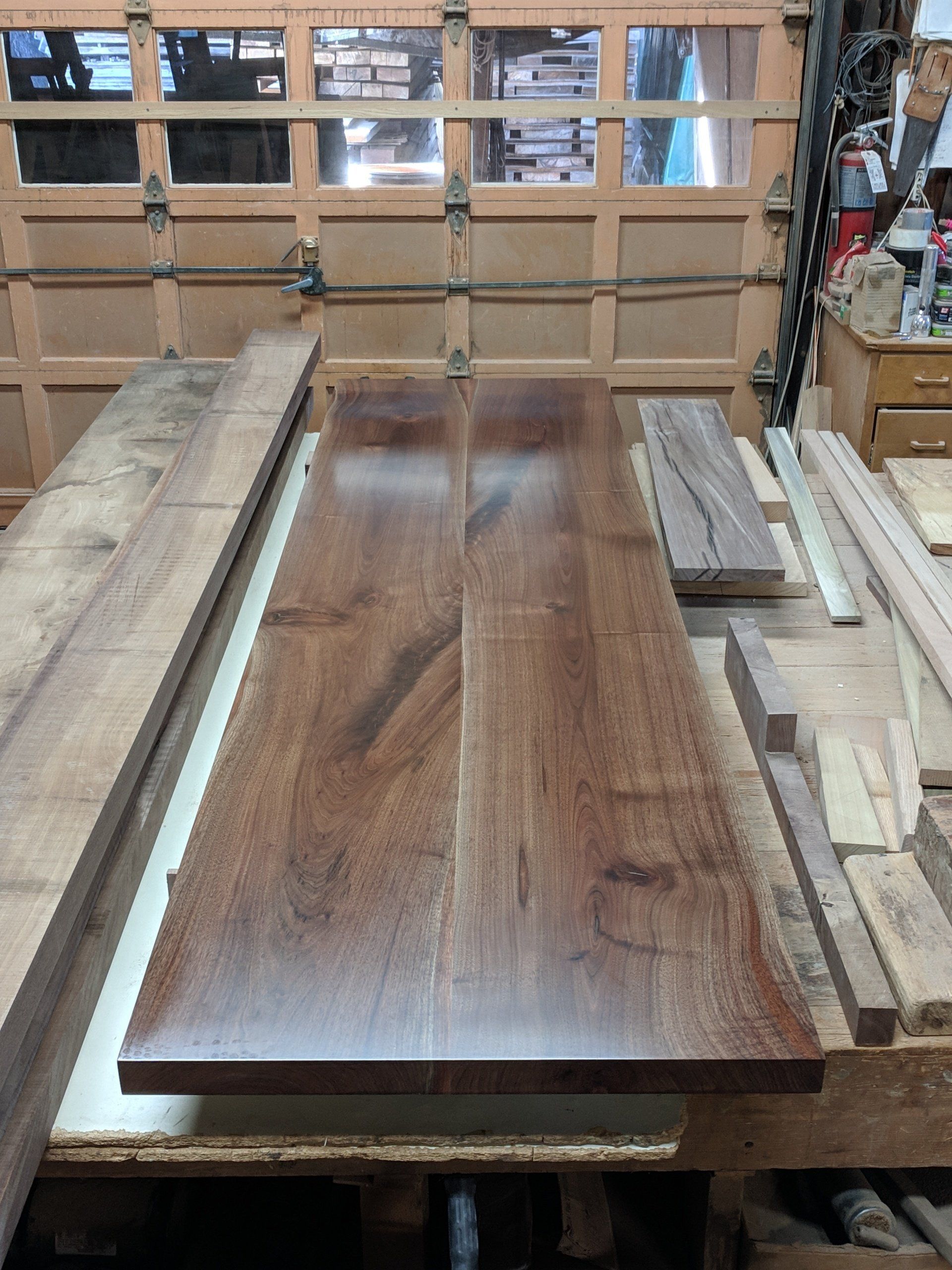 A finished, dark brown wooden tabletop sits on a workbench in a workshop.