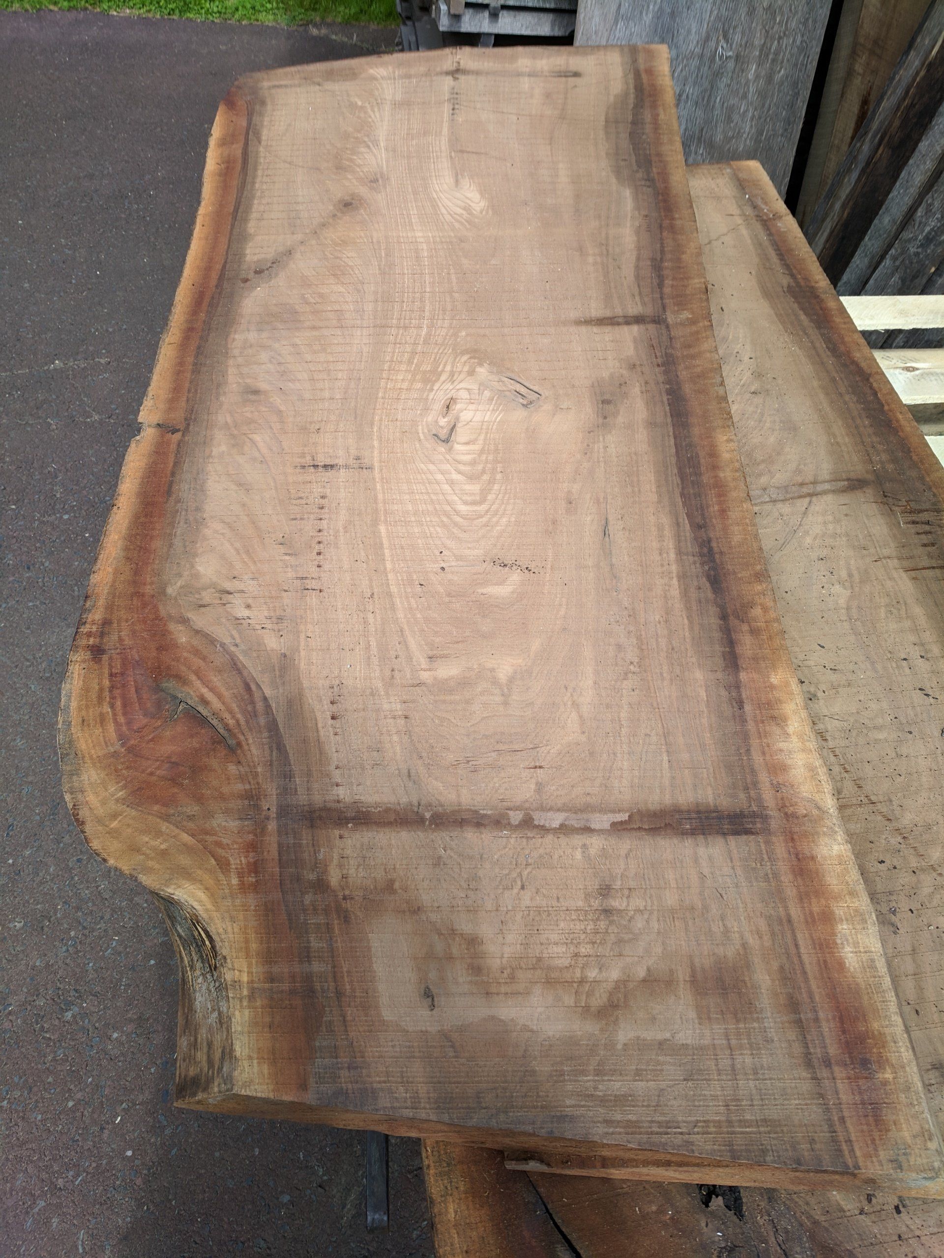 Two brown wood slabs with live edges, lying outdoors.