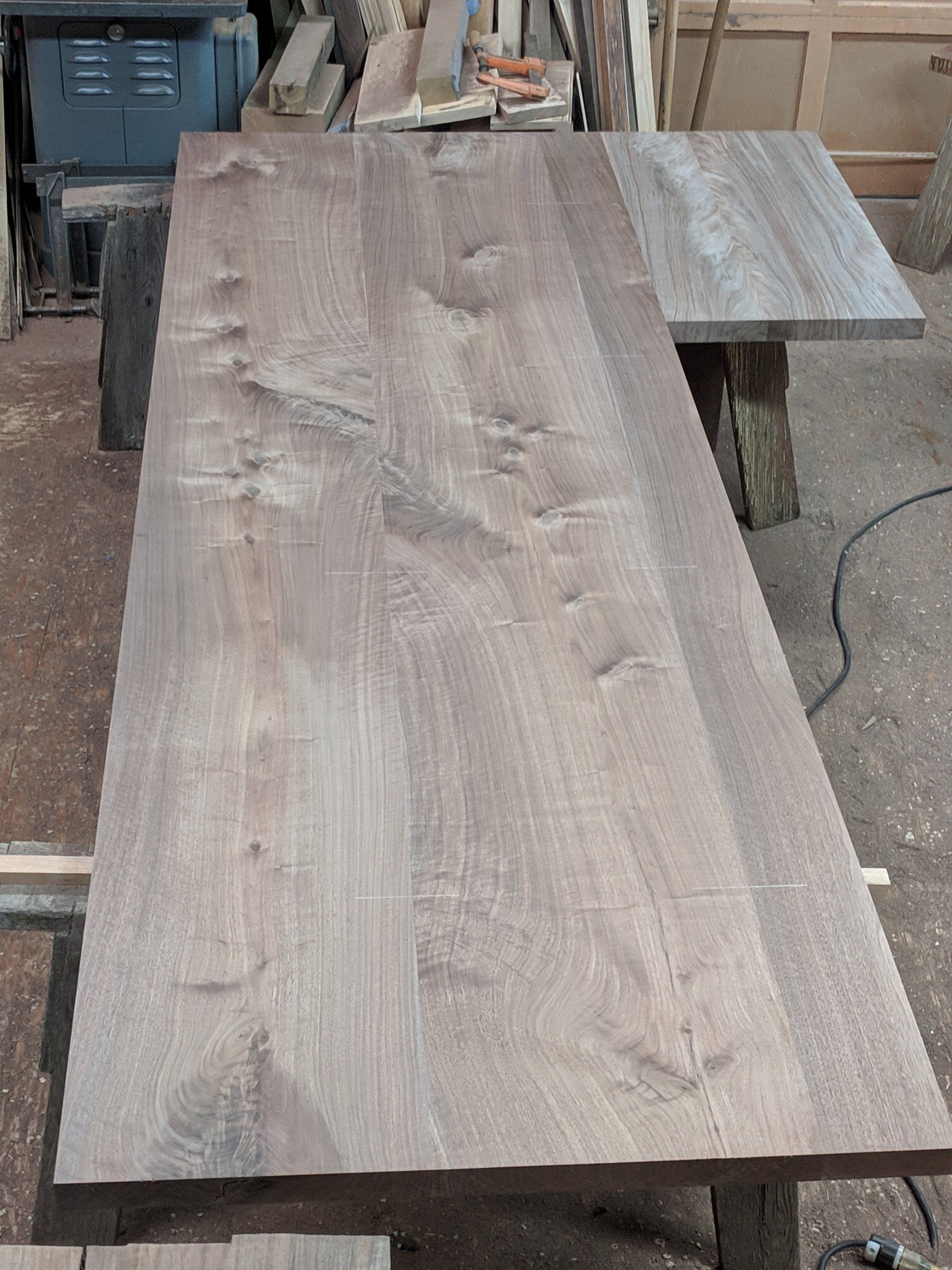 Wooden tabletop, light brown, with knot patterns and a smaller attached piece, on sawhorses.
