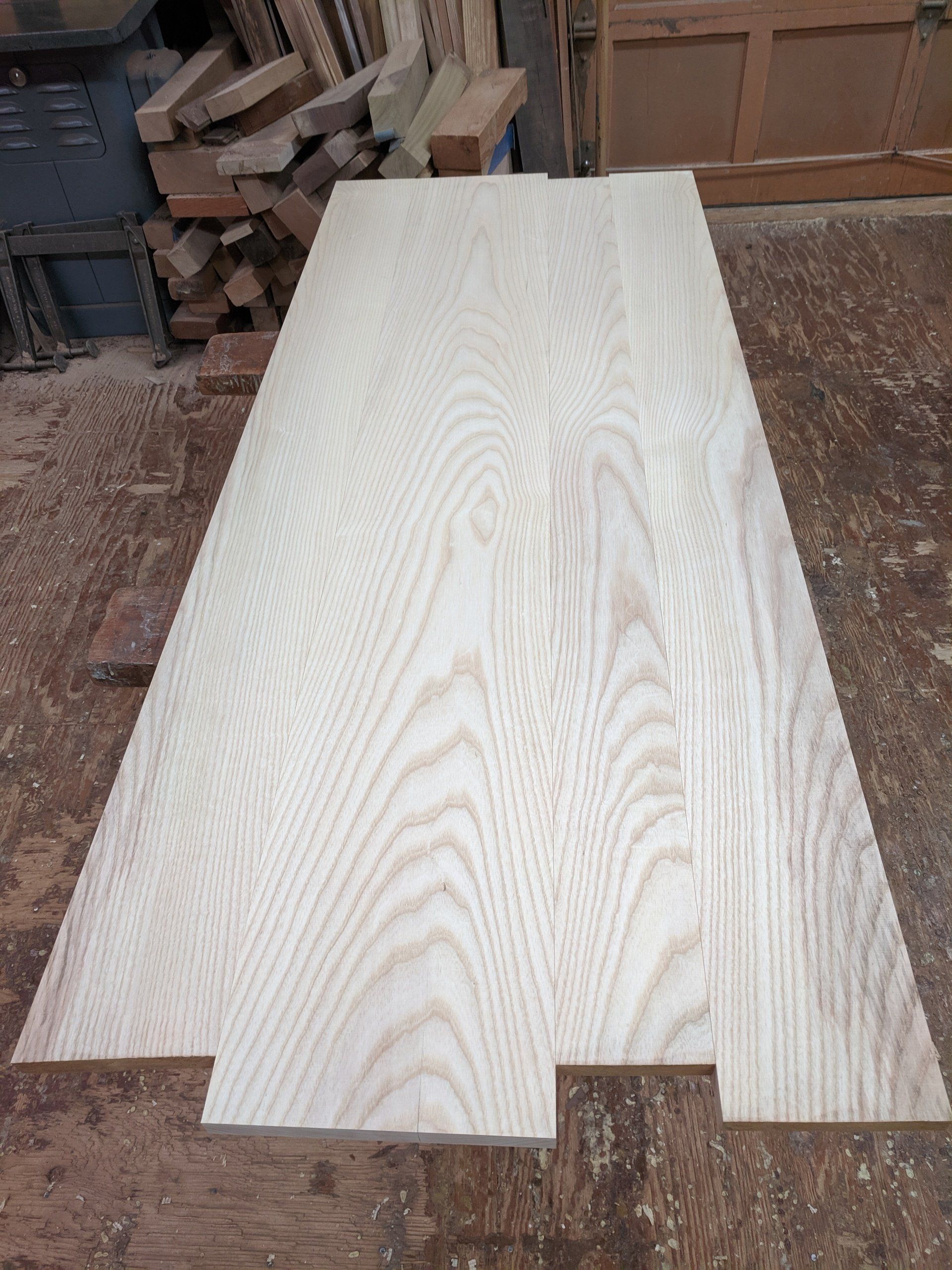 Light-colored, wide wooden planks with visible grain, laid out on a workshop floor.