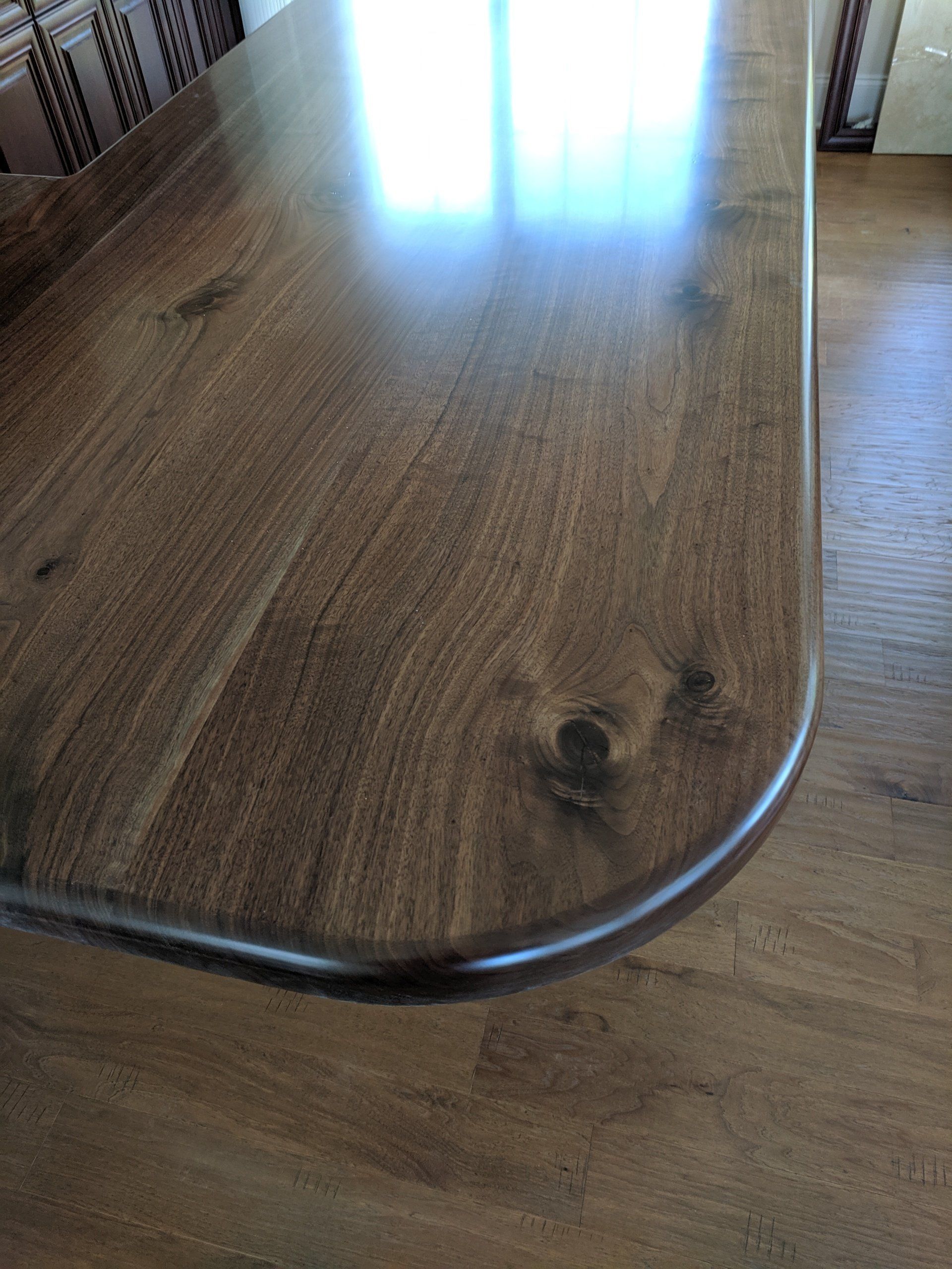 Close-up of a polished wooden table with rounded corners, reflecting light. Brown tones.