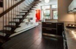 Modern kitchen with dark cabinetry, stairs, and hardwood flooring. Bright red wall visible.