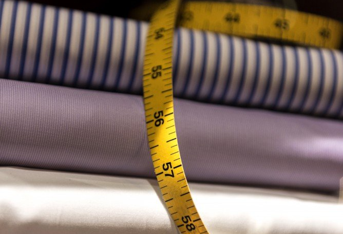 Yellow measuring tape draped over stacked fabric rolls of blue striped, purple, and white cloth.