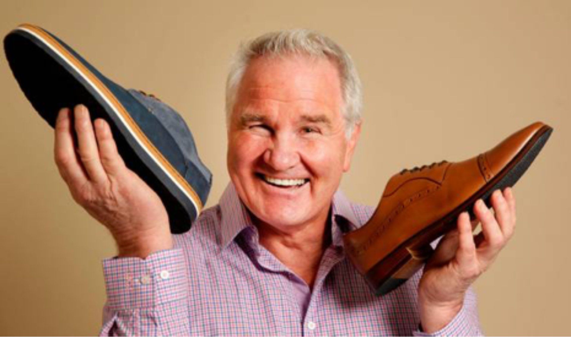 Man holding up a blue suede shoe and a brown leather dress shoe, smiling.