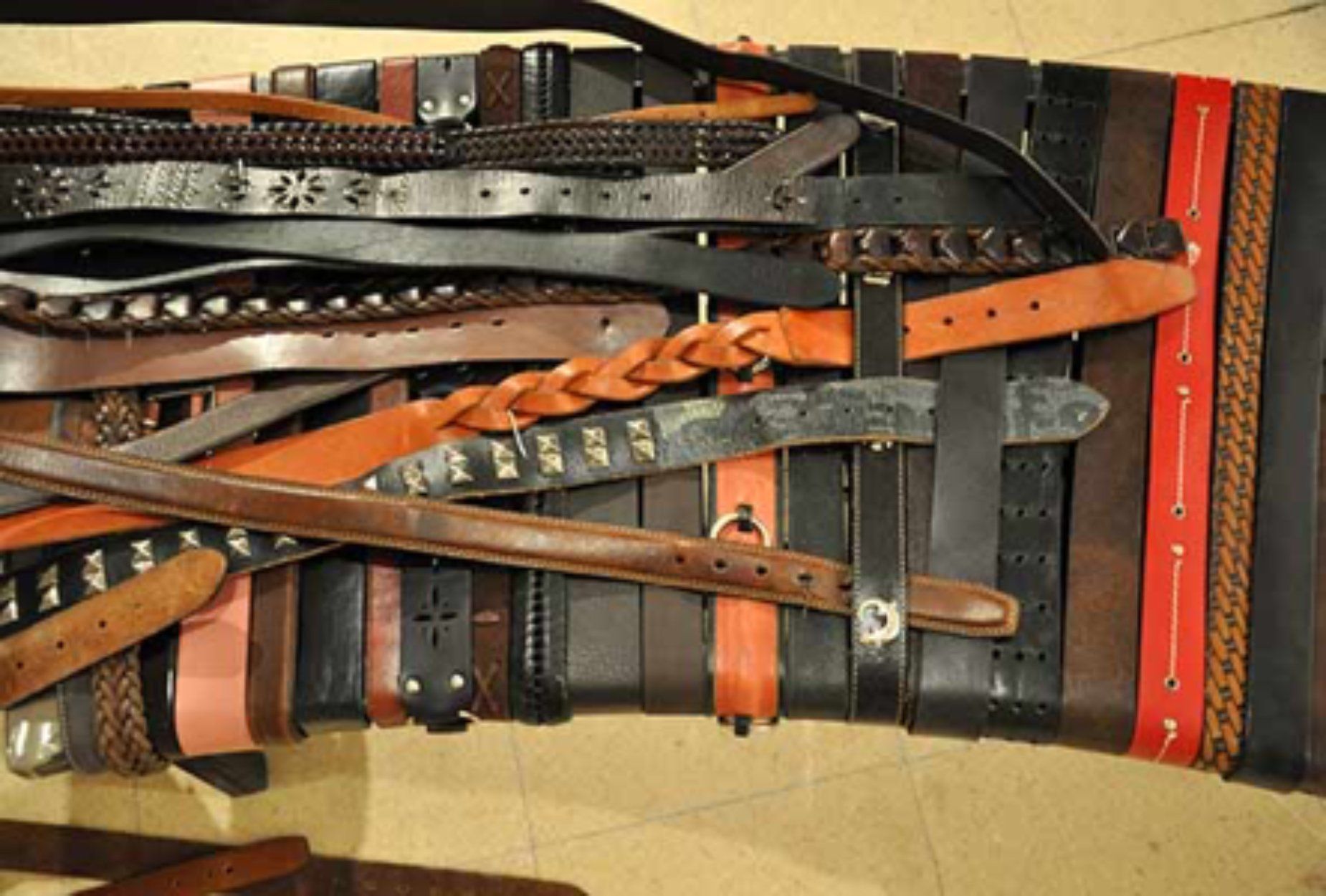 Collection of leather belts of various colors and styles, overlapping.