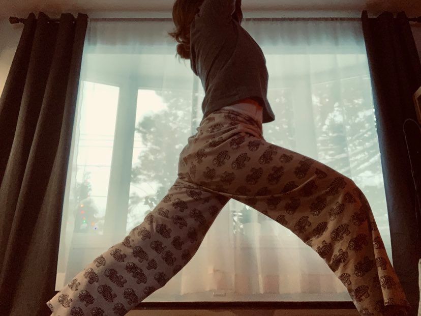 A woman in pajamas is doing a yoga pose in front of a window.