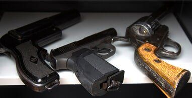 Three handguns displayed on a shelf: two semi-automatics and a revolver.