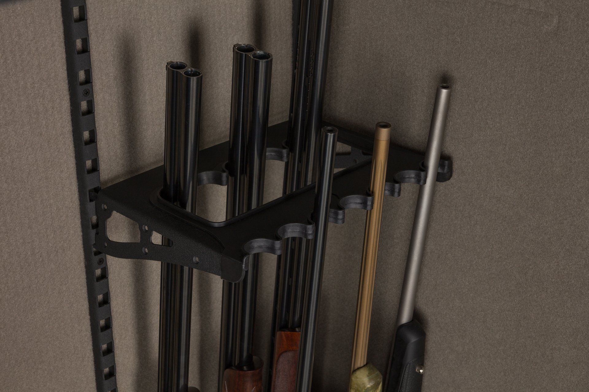 Black gun rack holding several long guns, with barrels of various sizes and colors.