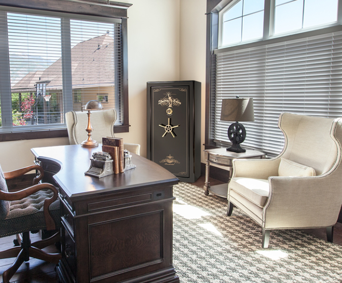 Elegant home office with a dark wood desk, two armchairs, a safe, and a window with blinds.