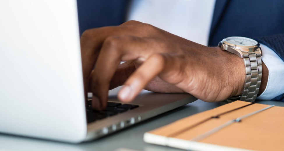 A man wearing a watch is typing on a laptop computer.