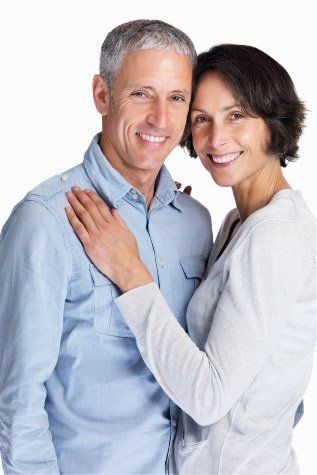 Smiling middle-aged couple posing together; woman's arm around the man's shoulder. They both look at the camera against a white background.