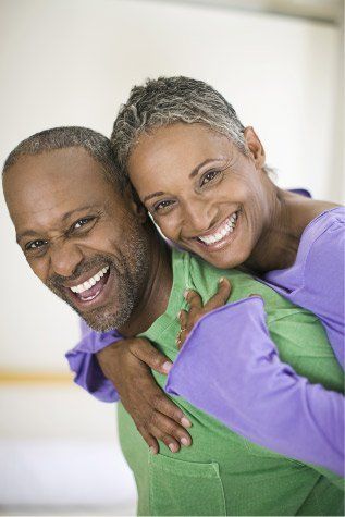 Smiling Black man giving a piggyback ride to smiling Black woman; indoors, bright light.