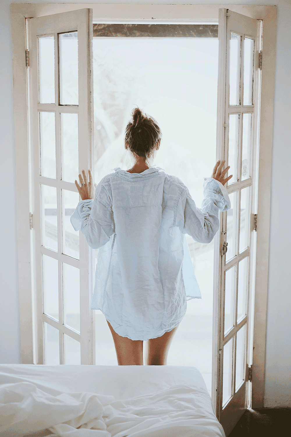 A woman in a blue shirt is standing in front of a window.