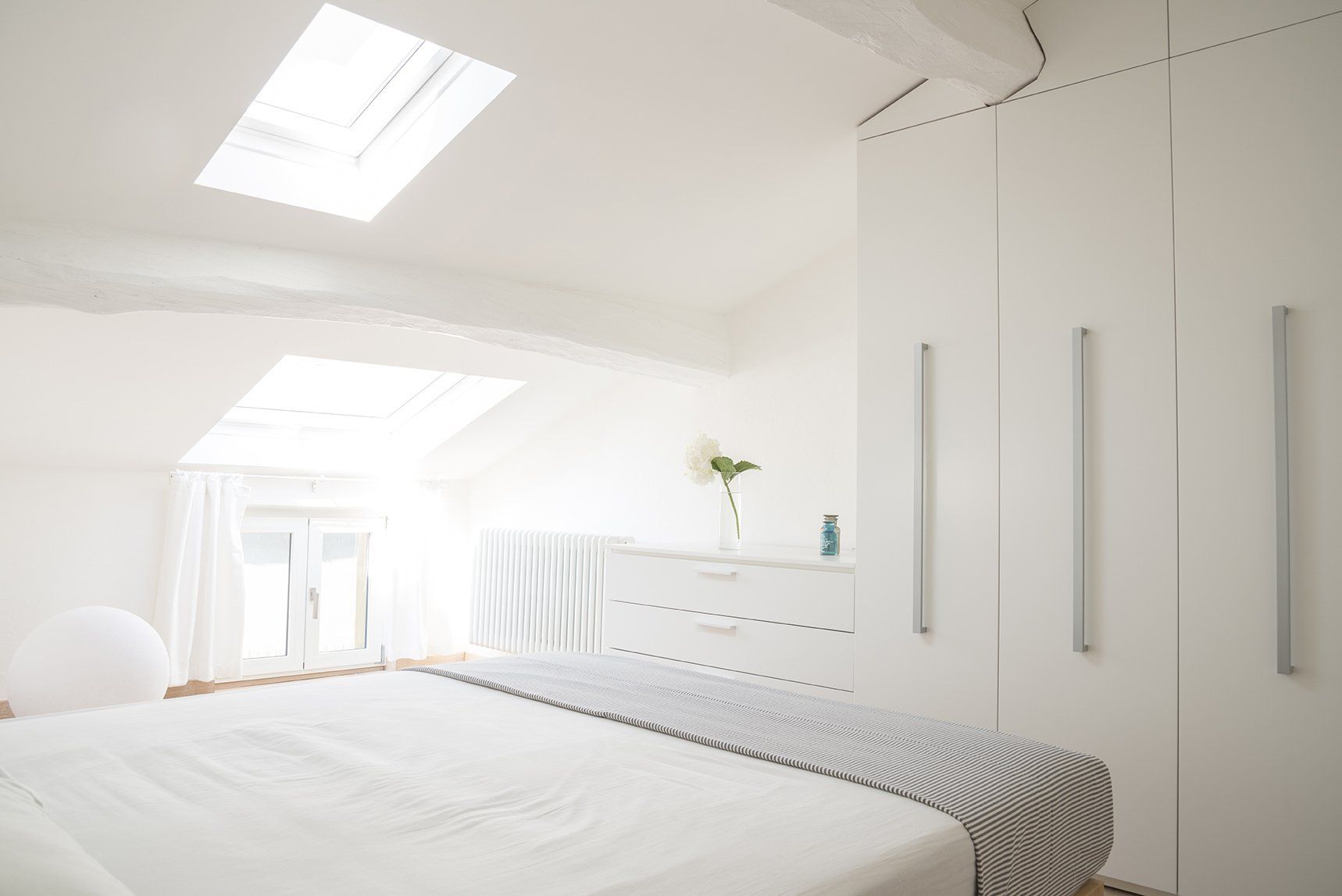 A bedroom with a bed , dresser , and skylight.