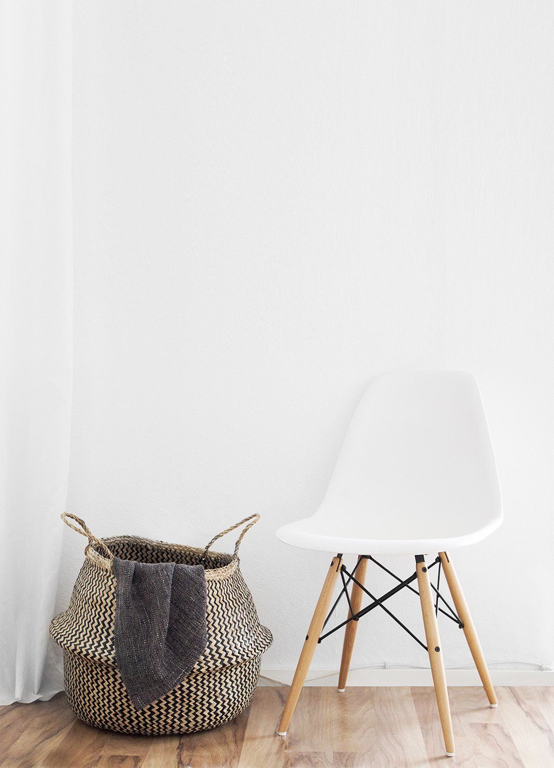 A white chair is sitting next to a basket on a wooden floor.