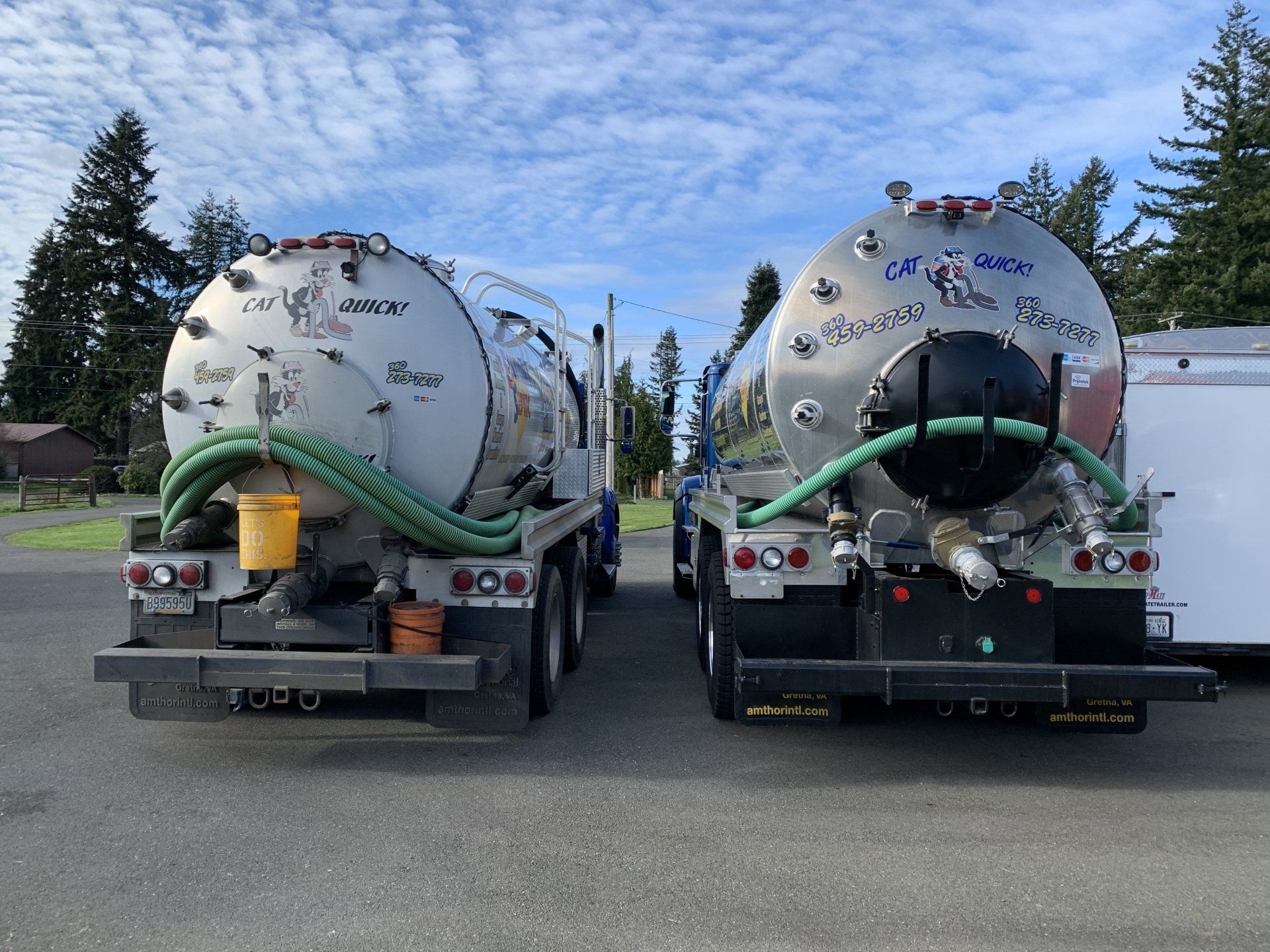 Two silver septic trucks parked outdoors against a blue sky.
