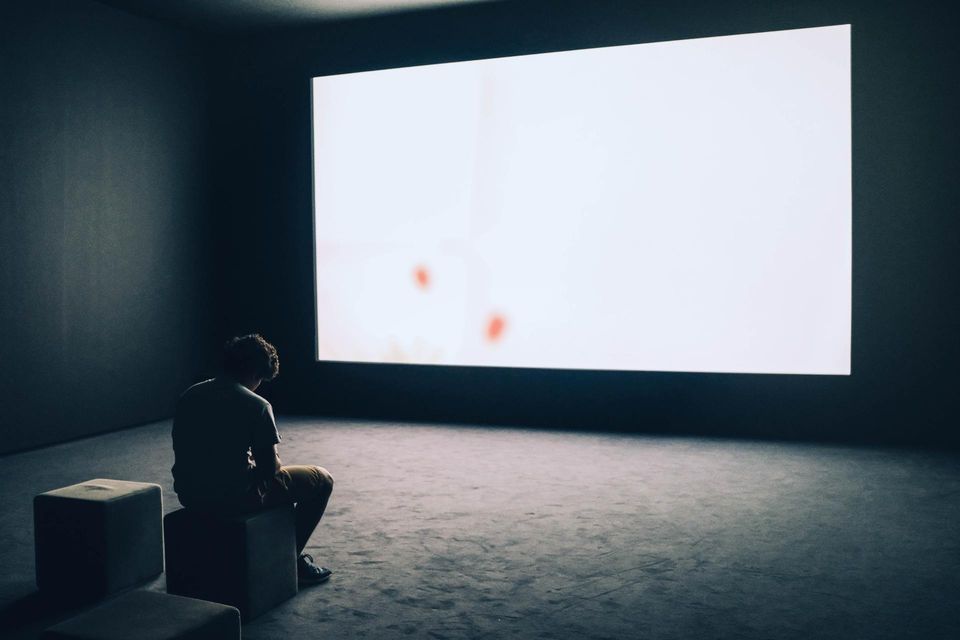a men sitting in the dark in front of a white screen