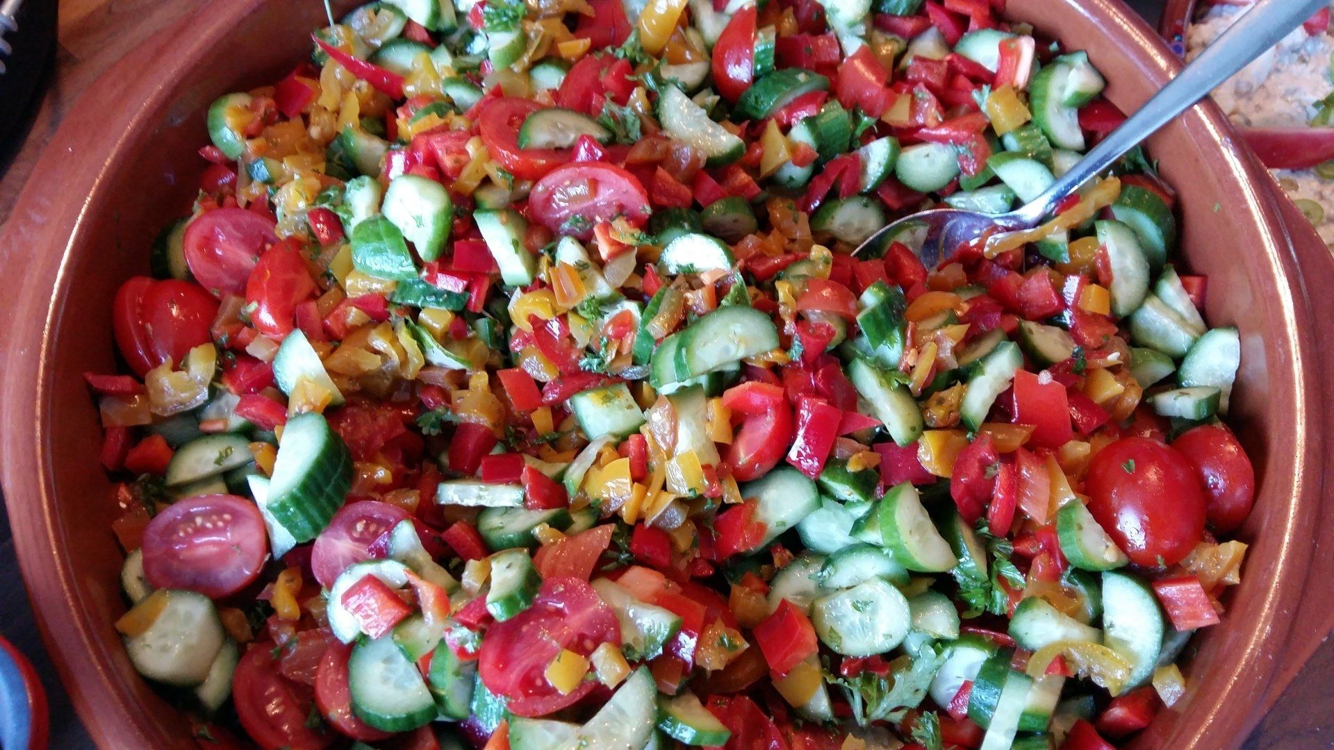 Een kom met een slade van tomaten, komkommers en paprika's in een terracotta schaal.