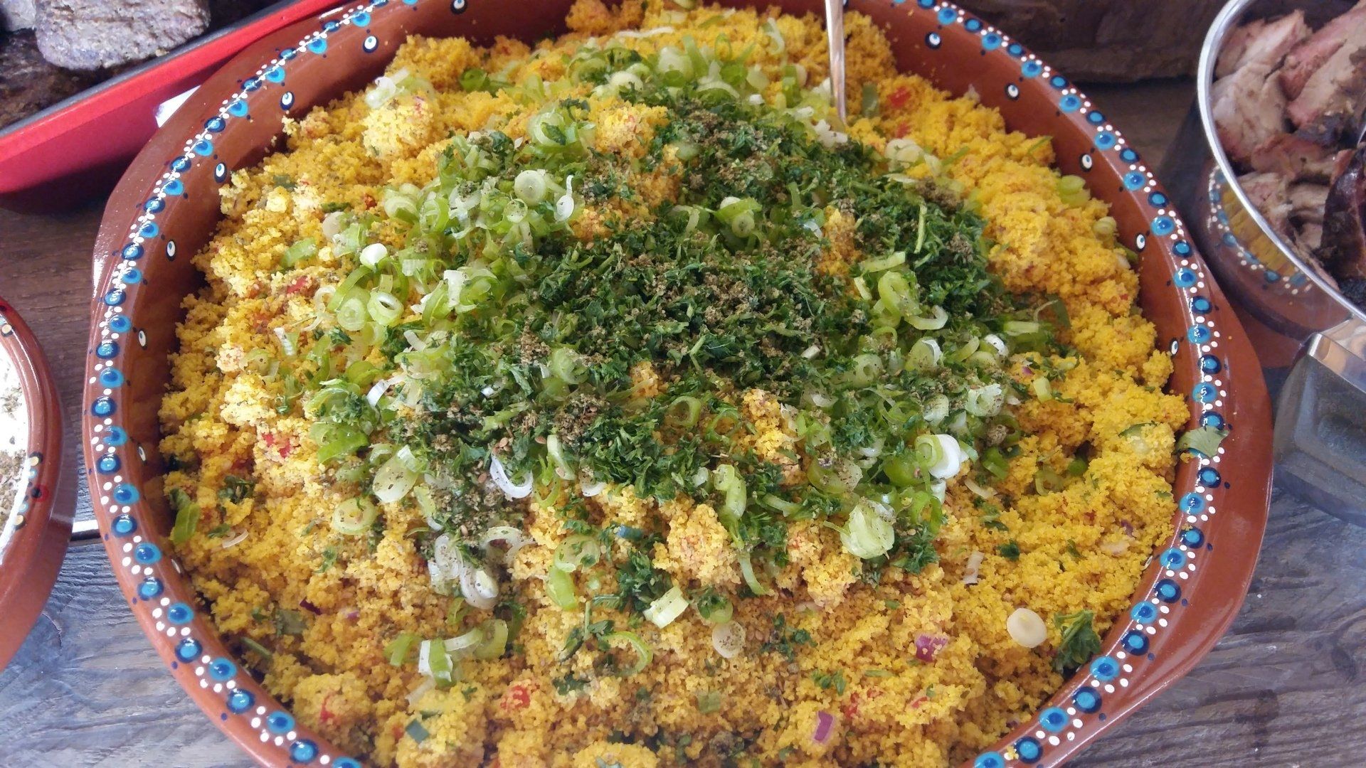 Een kom gele couscous, gegarneerd met fijngehakte groene kruiden en lente-uitjes.