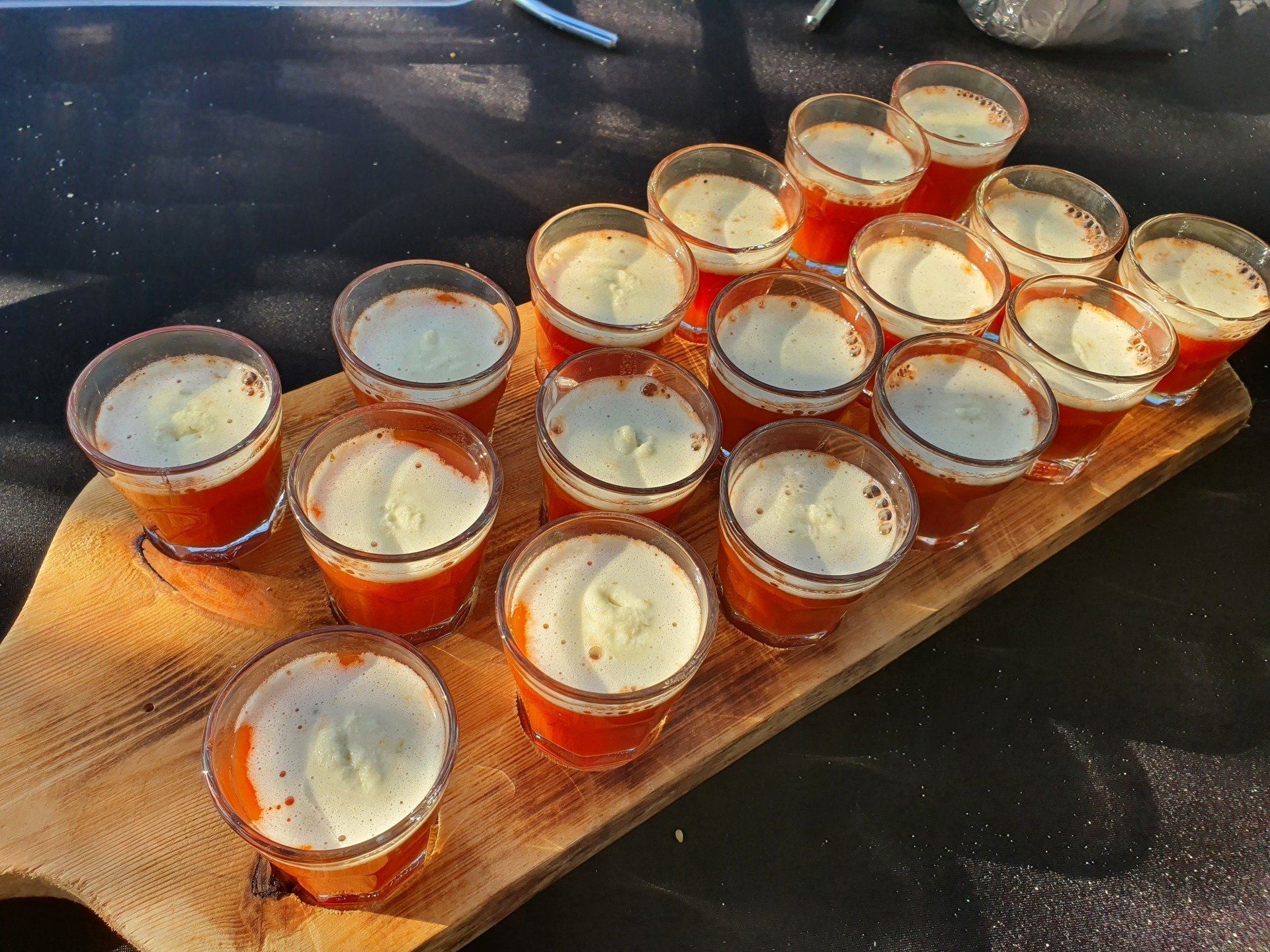 Kleine glaasjes met tomatenbouillon met rozemarijncreme, op een houten serveerplank.