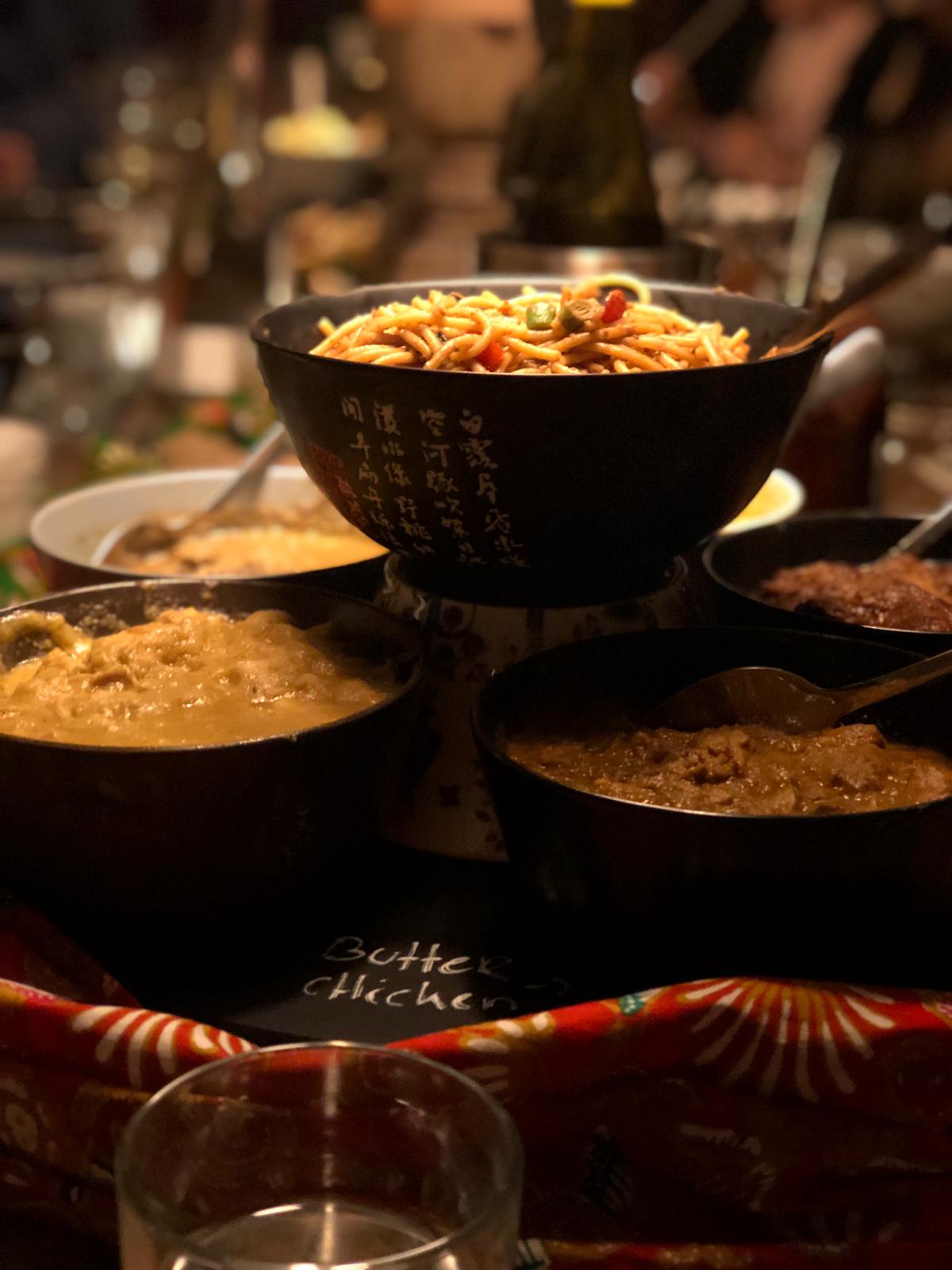 Schalen met diverse gerechten, waaronder noedels en curry's, op een etagère.