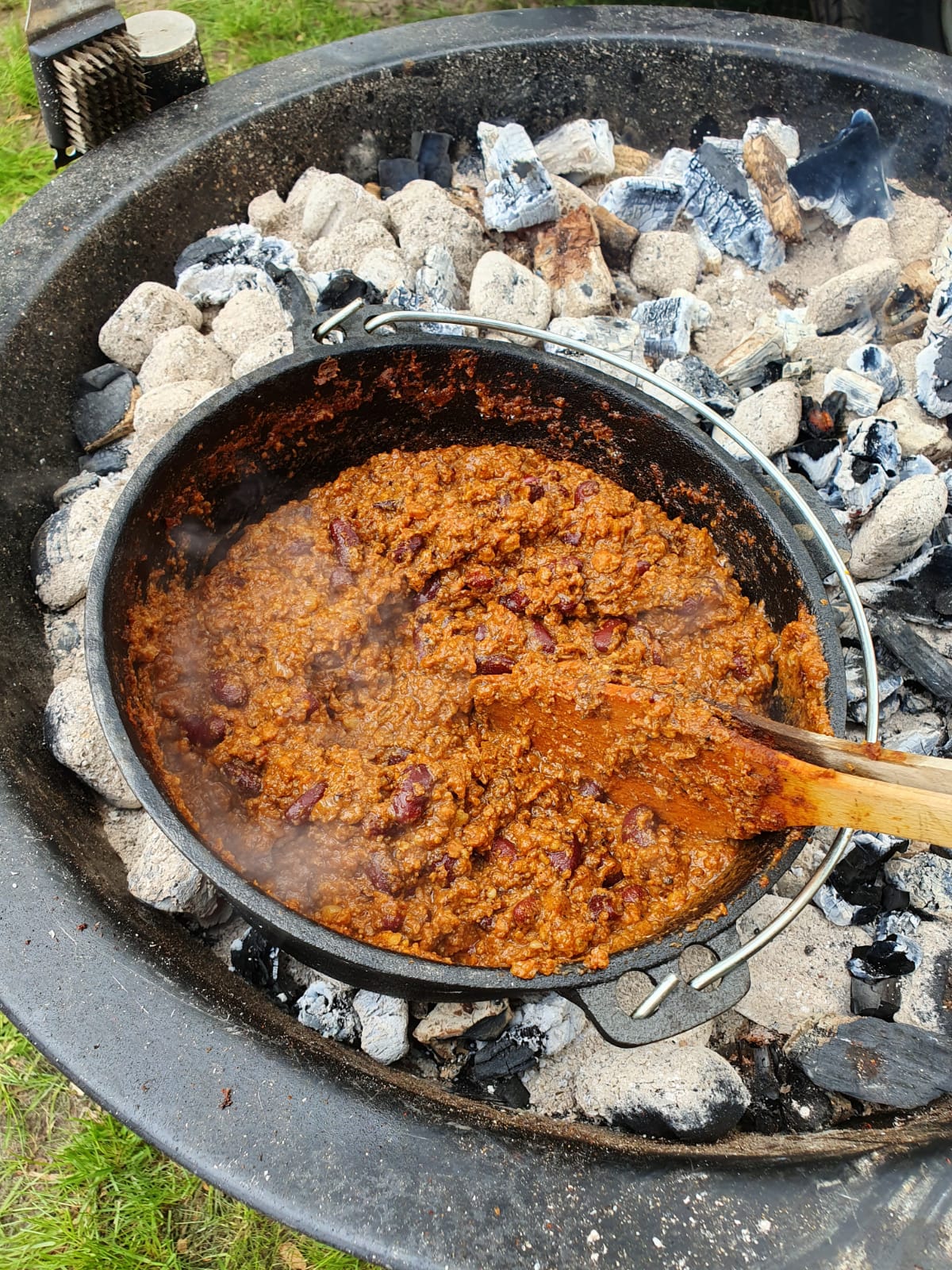 Chili con carne wordt gekookt in een braadpan boven hete kolen in een vuurkuil.