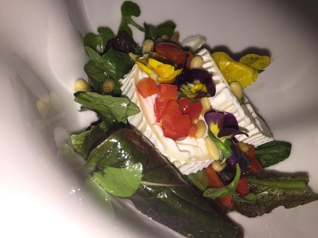 Salade met geitenkaas, tomaten, pijnboompitten en eetbare bloemen op een wit bord.