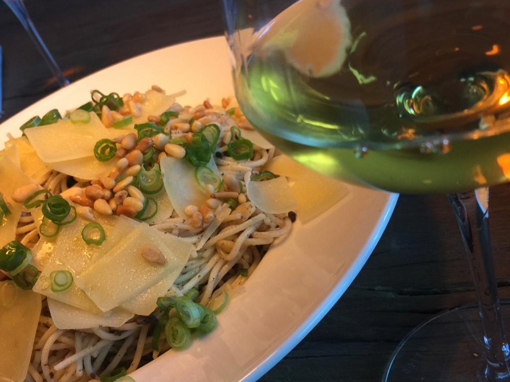 Een bord noedels met diverse toppings, naast een glas witte wijn.