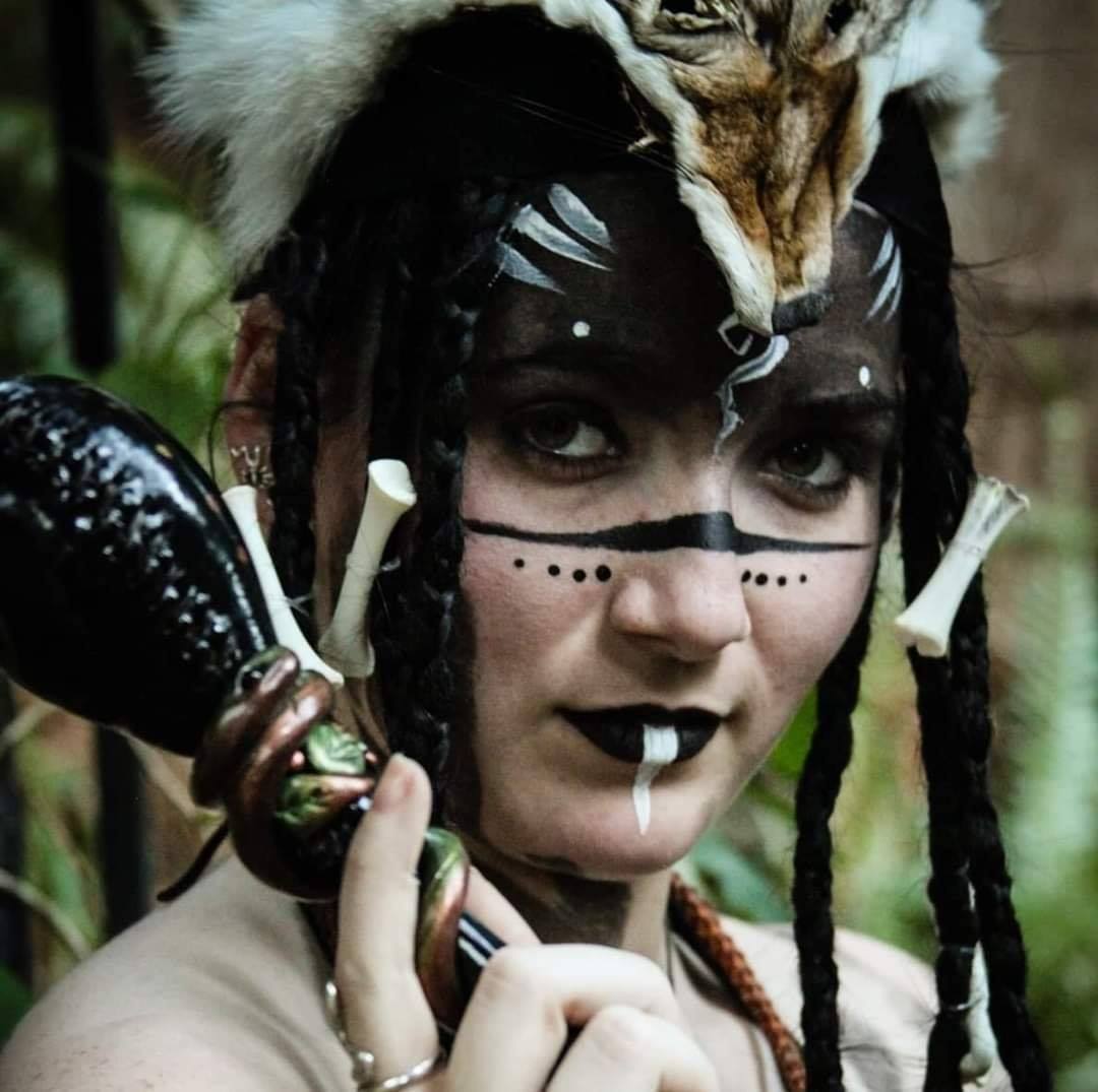 A woman with bones in her hair and holding a totem in her hand