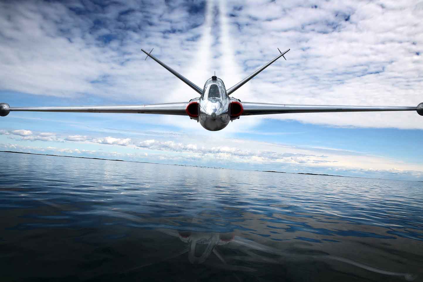 A fighter jet is flying over a body of water.