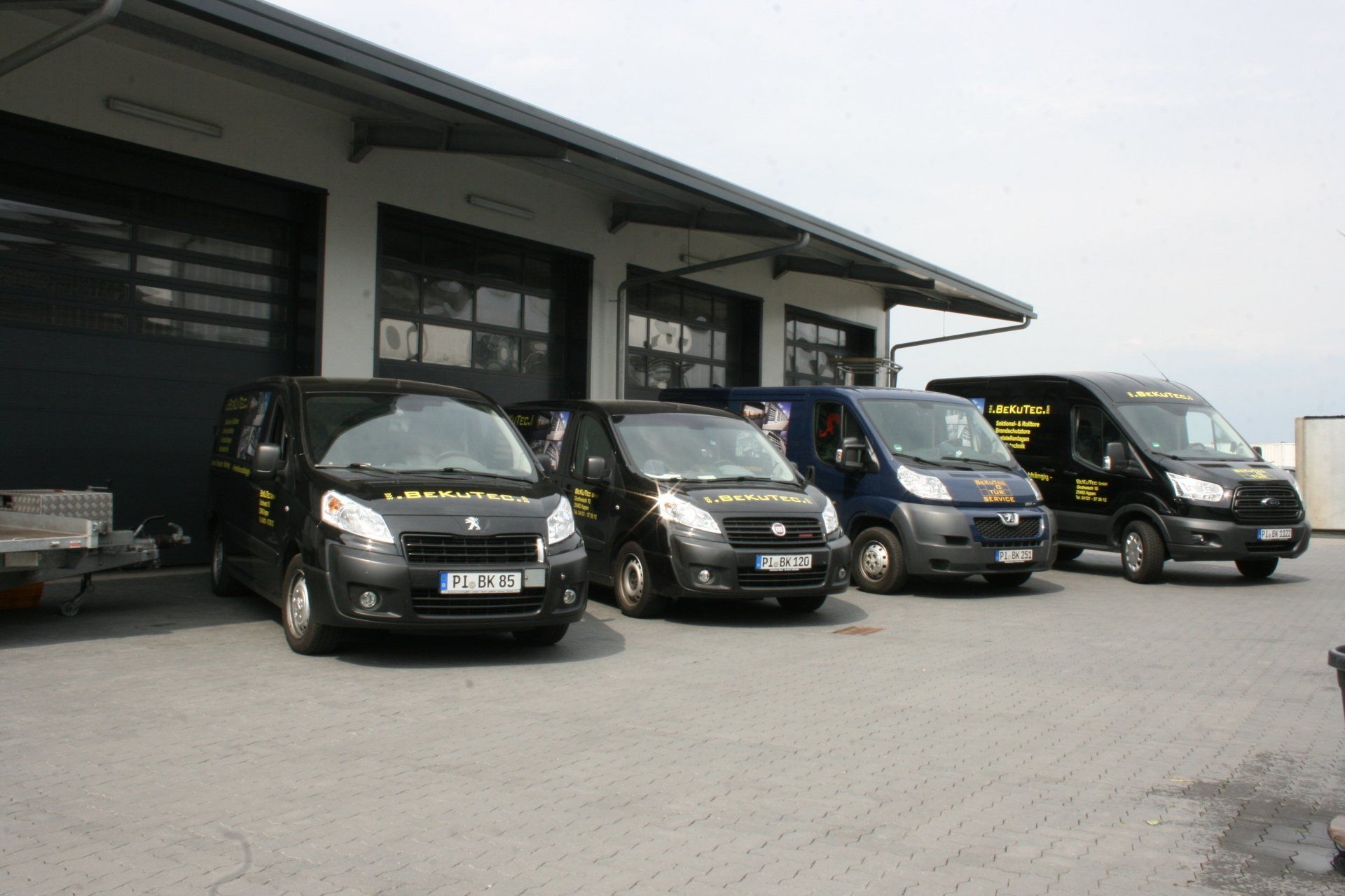 Vier schwarze Lieferwagen parkten vor einem Gebäude mit Garagentoren.