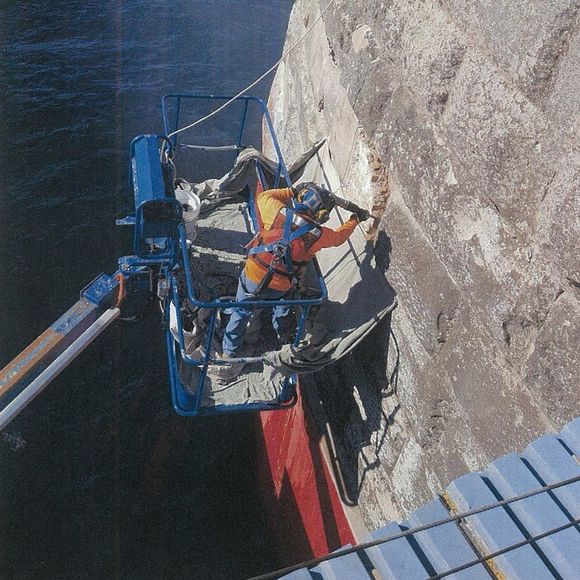 A man in a bucket is working on a wall