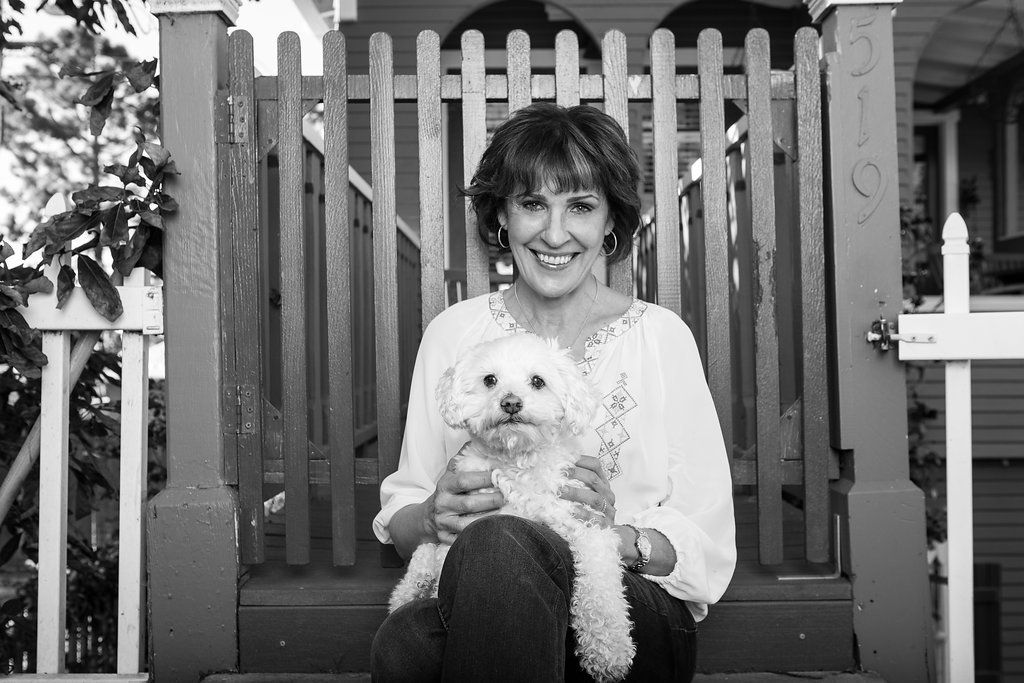 Woman sitting on a bench holding a small white dog in front of a wooden fence