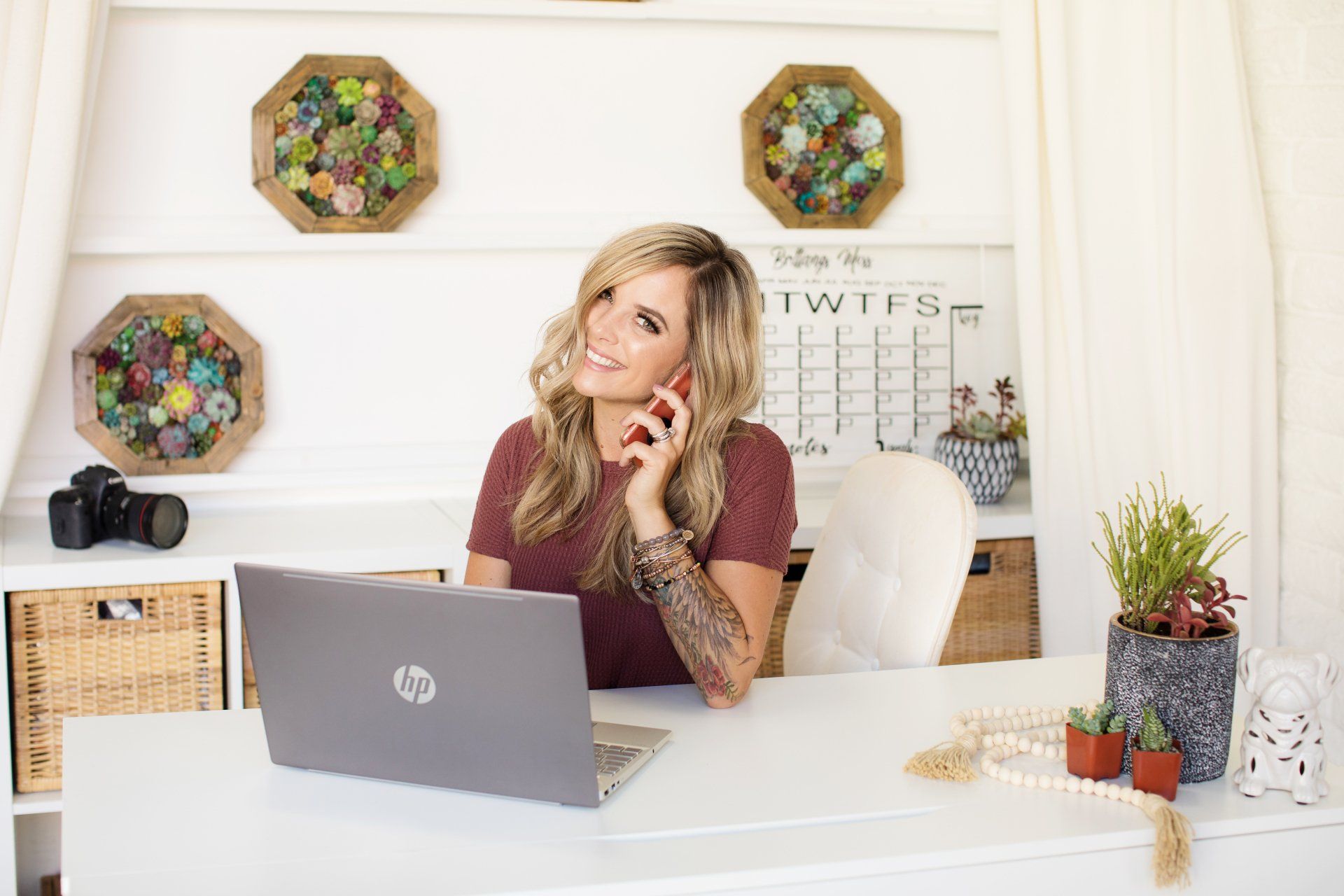 A woman is sitting at a desk with a laptop and talking on a cell phone.