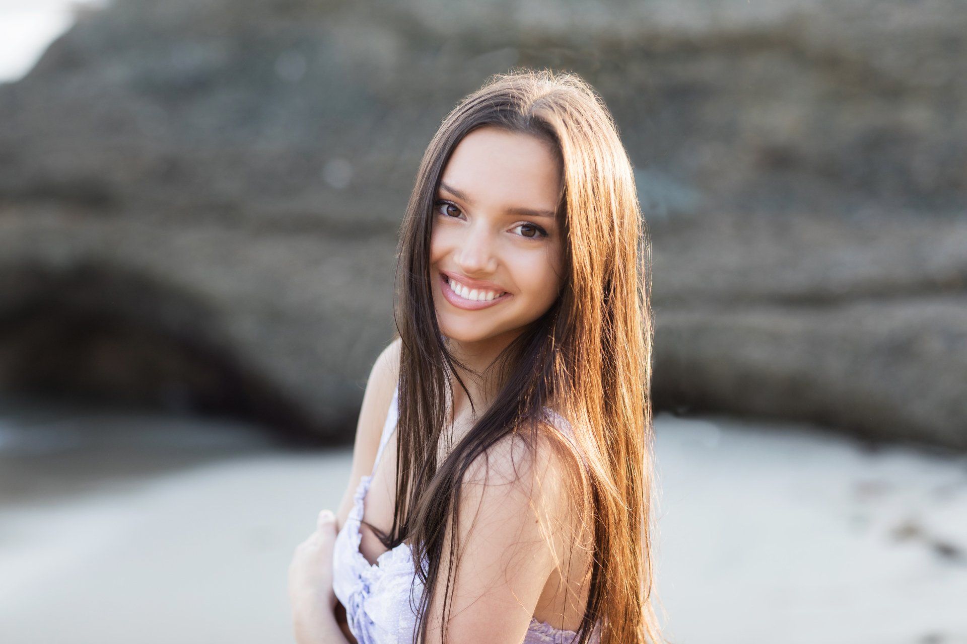 A woman with long hair is smiling on the beach.