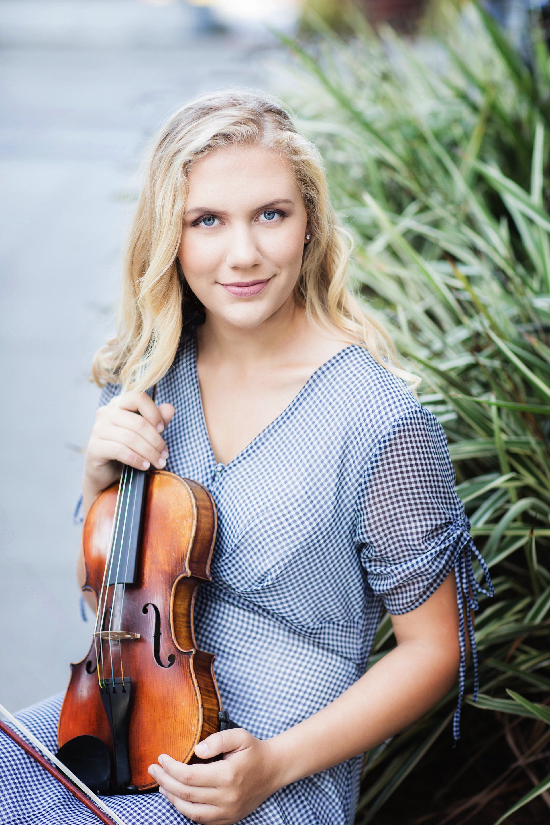 A young woman in a blue dress is holding a violin.