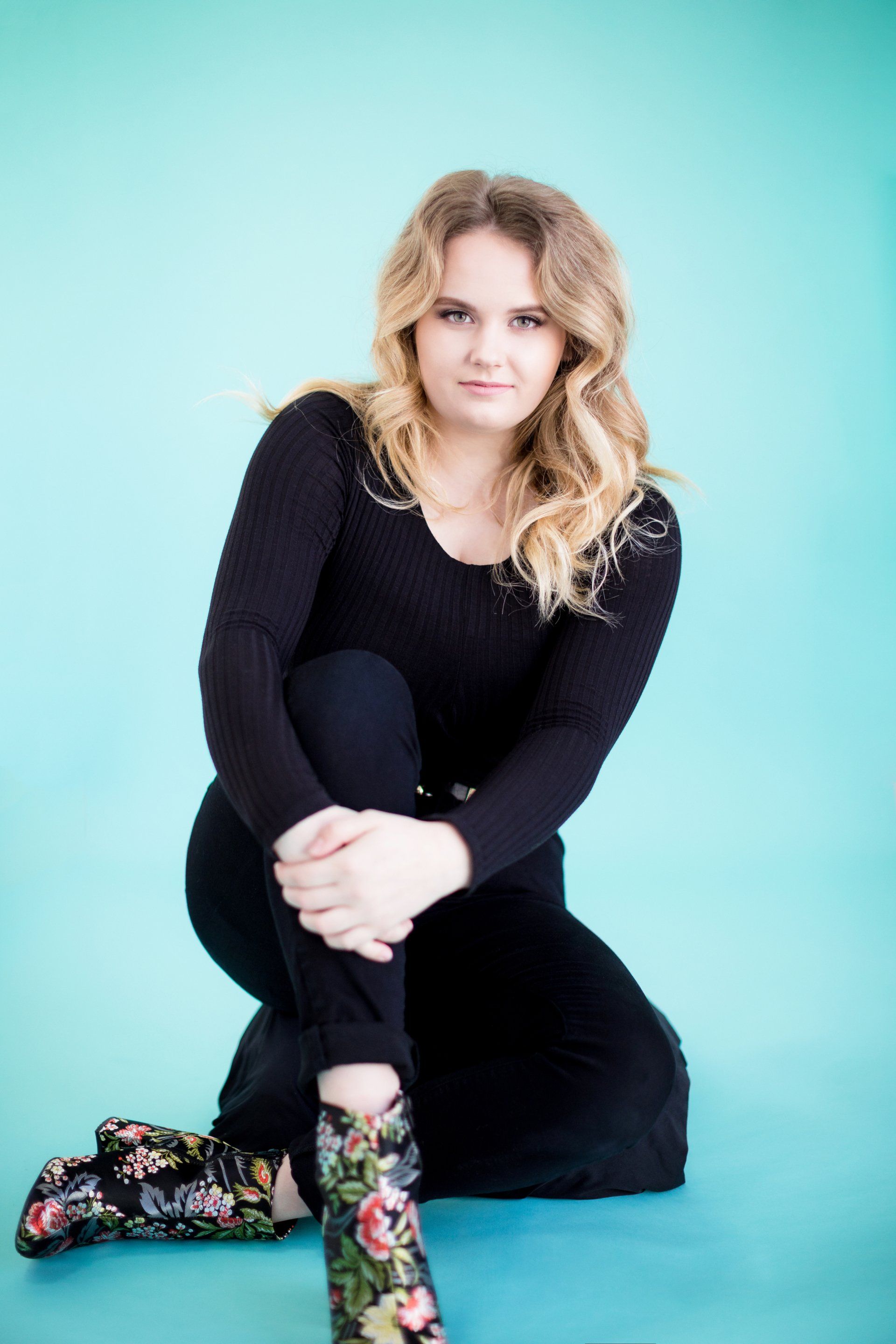 A woman in a black jumpsuit and floral boots is kneeling down.