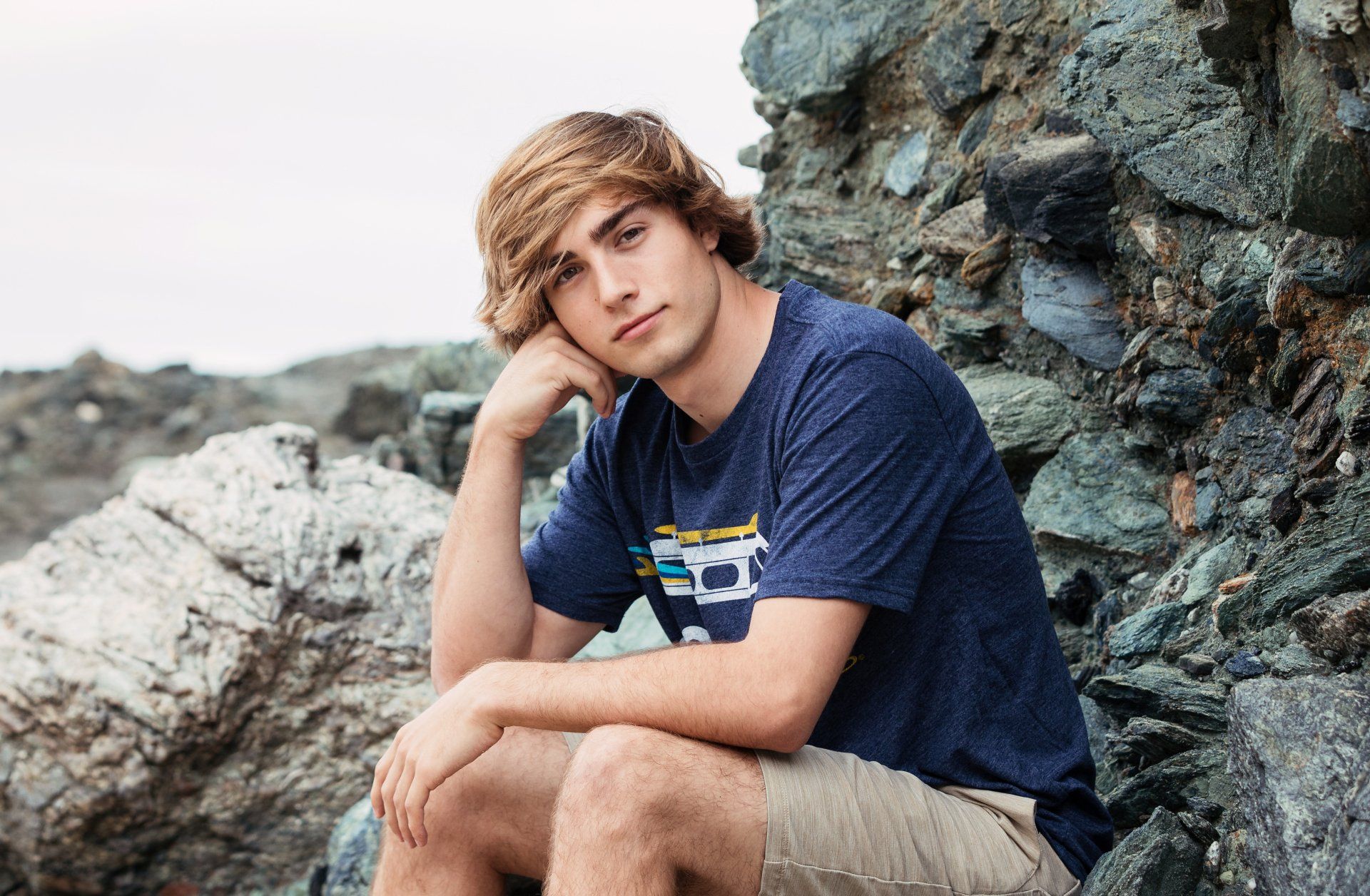 A young man is sitting on a rock with his head resting on his hand.