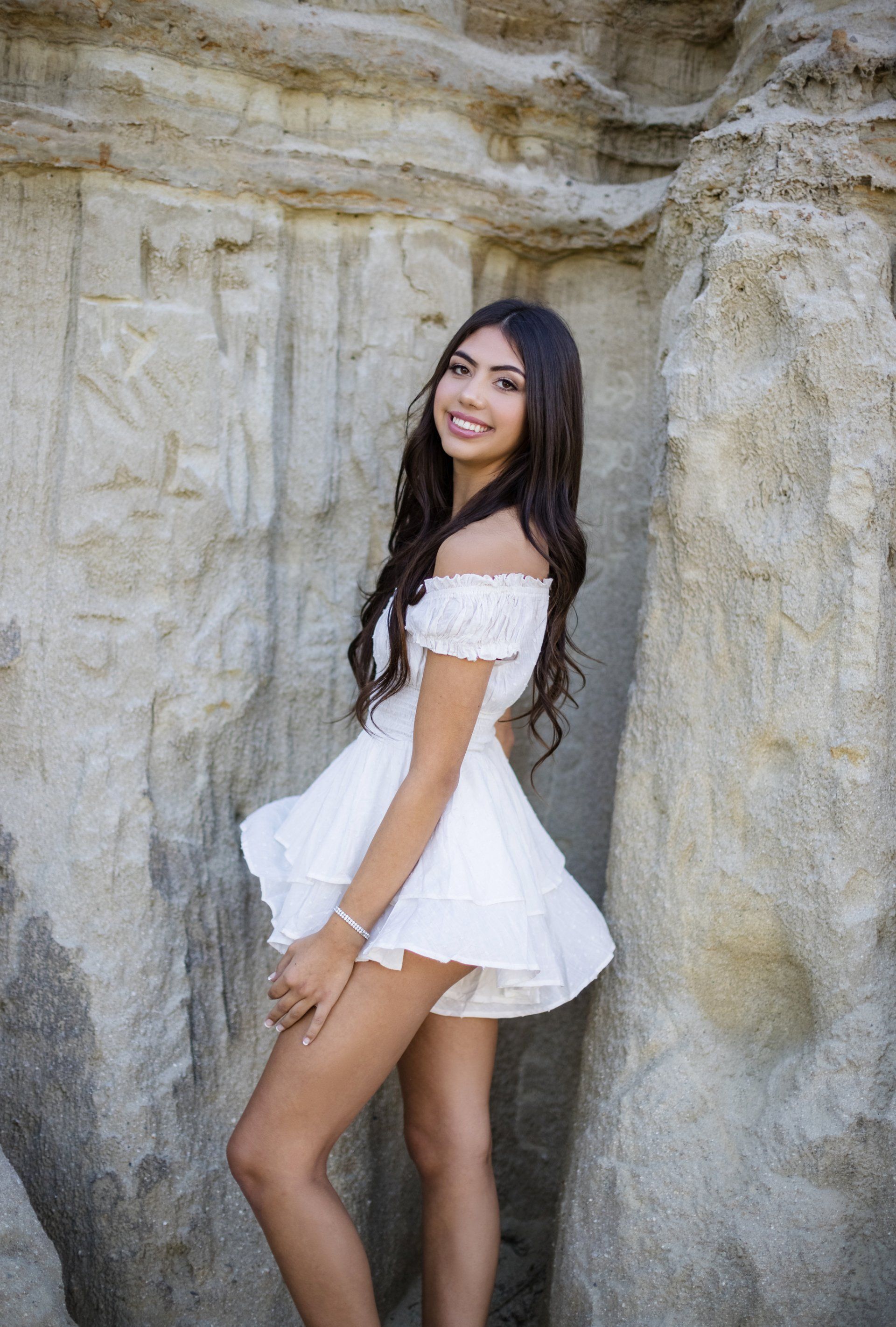 A woman in a white dress is standing next to a rock wall.