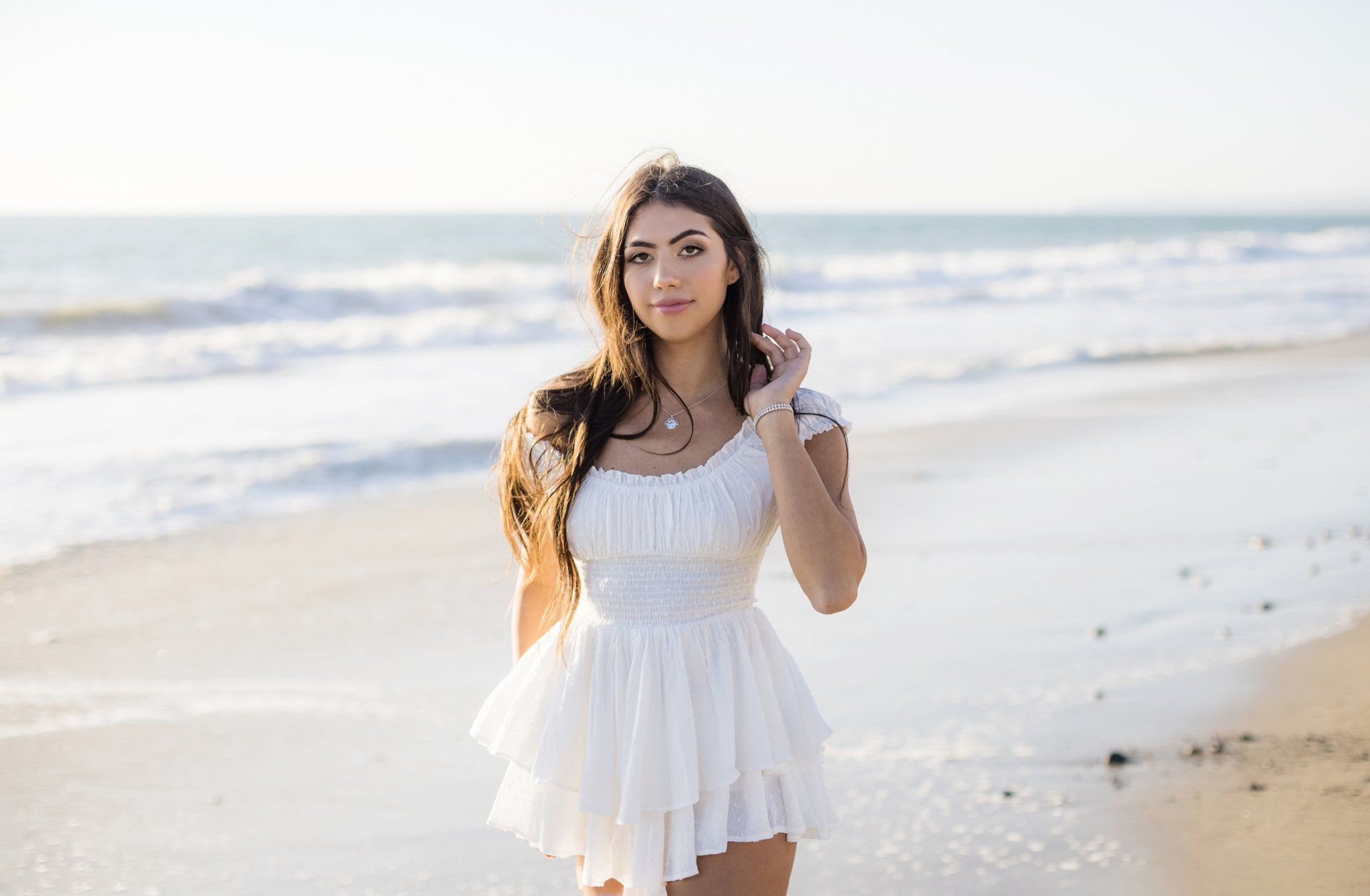A woman in a white dress is standing on the beach.