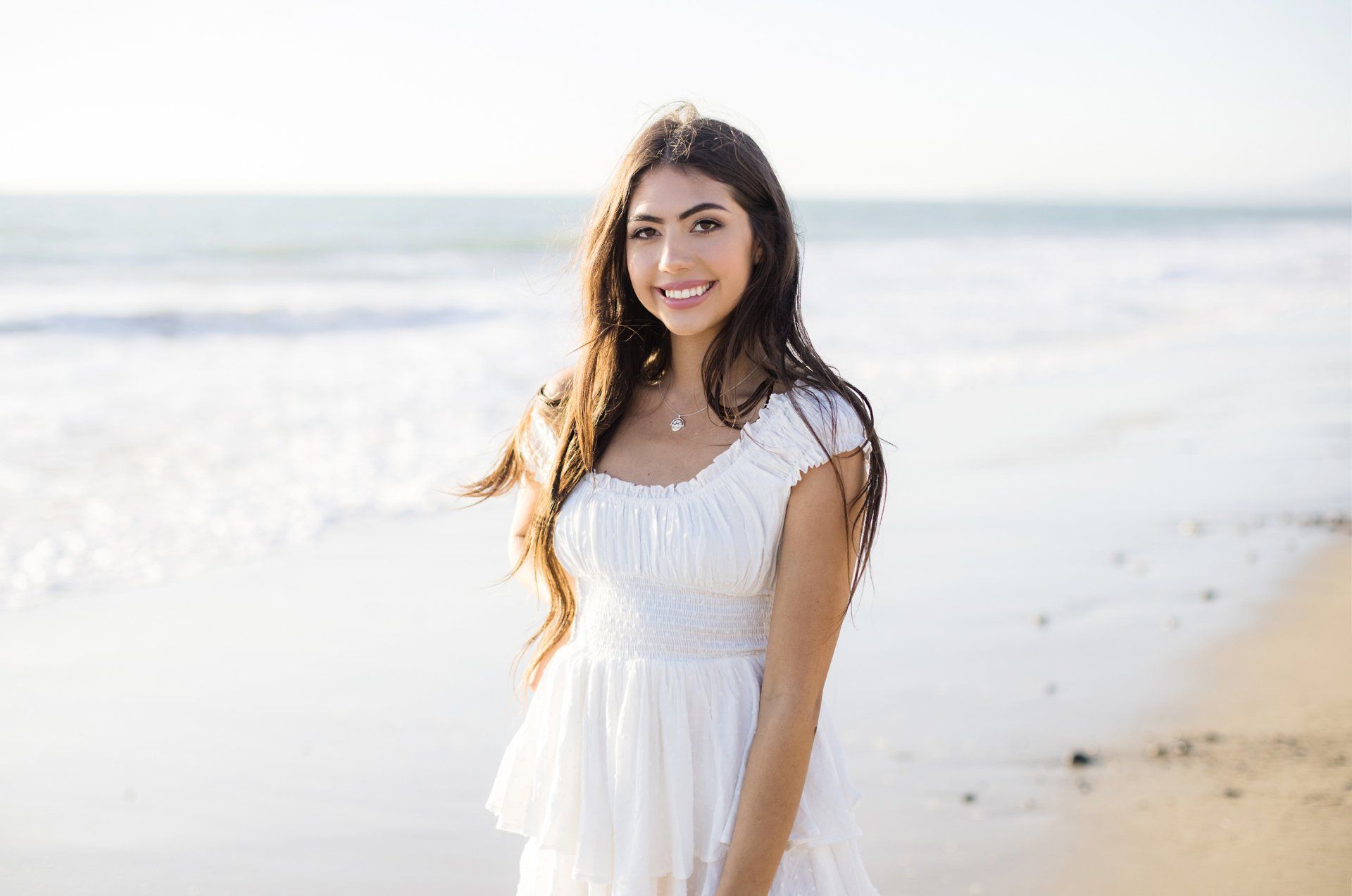 A woman in a white dress is standing on the beach.