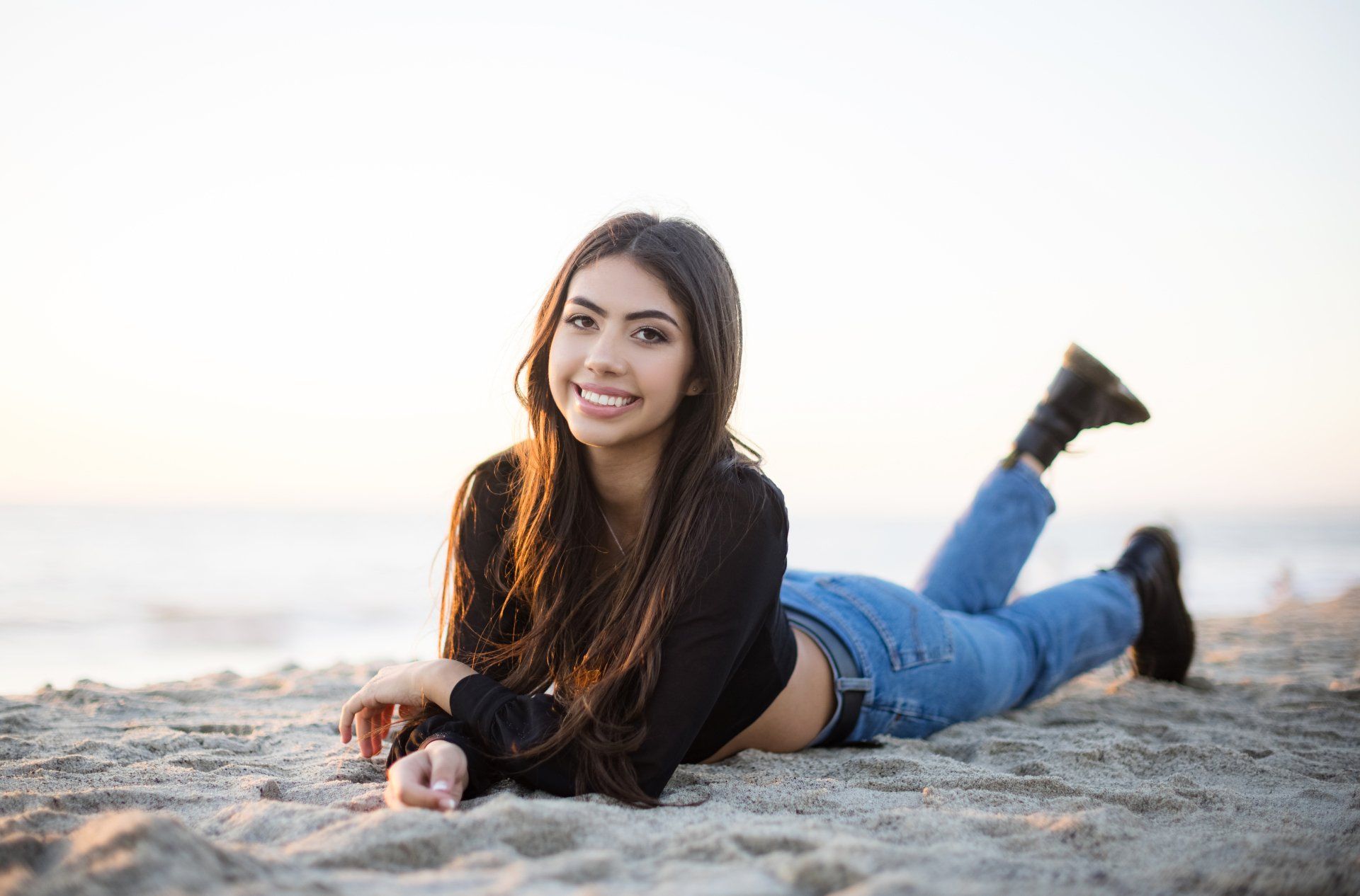 A young woman is laying on her stomach on the beach.