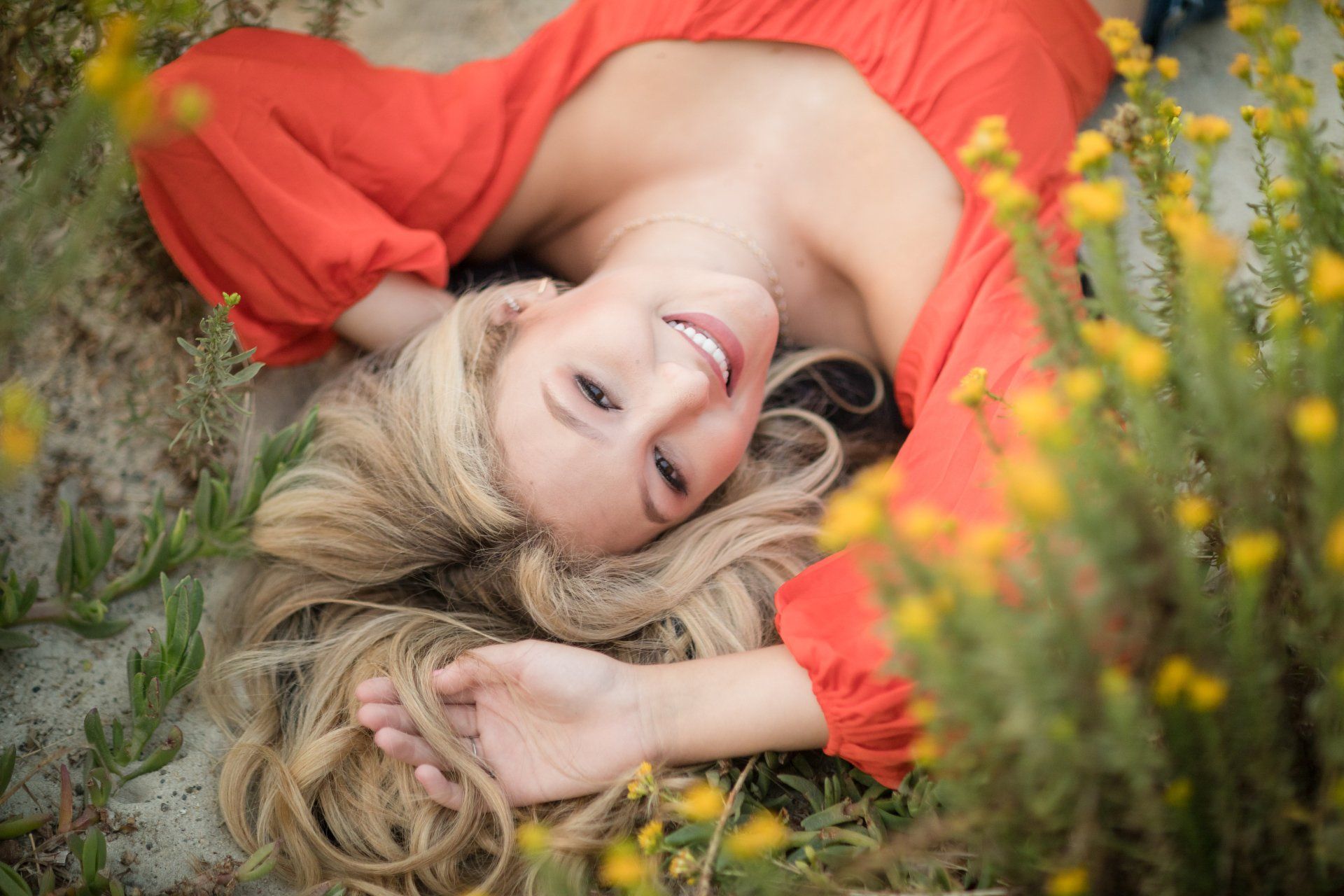A woman in a red dress is laying in a field of yellow flowers.