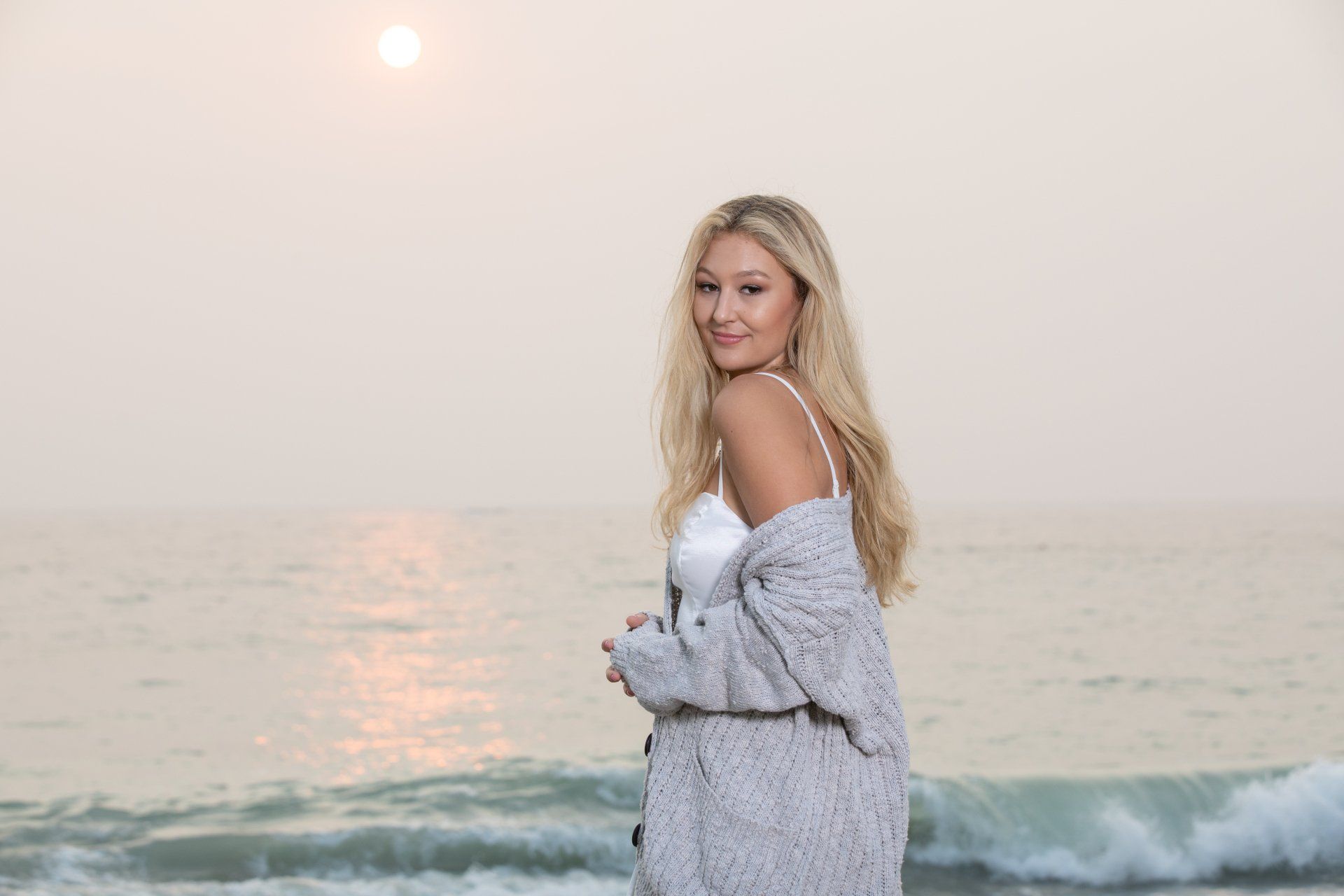 A woman is standing on the beach looking at the ocean.